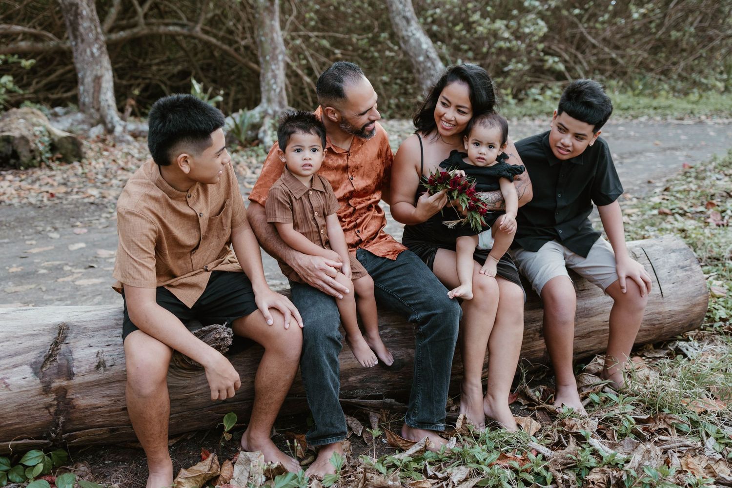 A family sits together on a fallen log in a natural outdoor setting during a casual photo session.