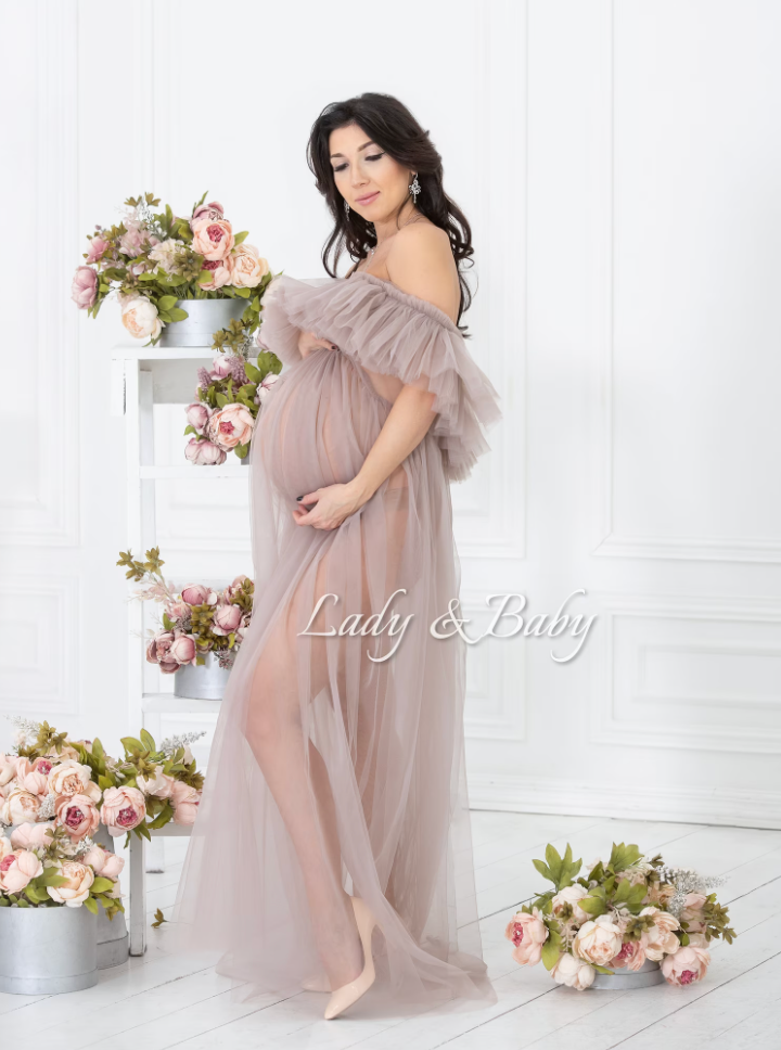 Romantic maternity portrait in flowing mauve tulle gown surrounded by pink floral arrangements.