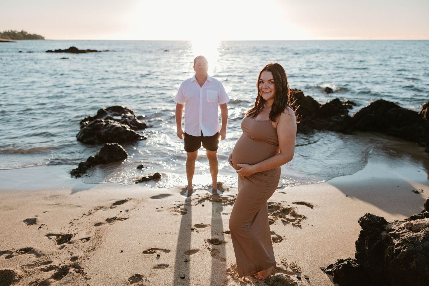 Maternity photo session on rocky beach at sunset with ocean waves.