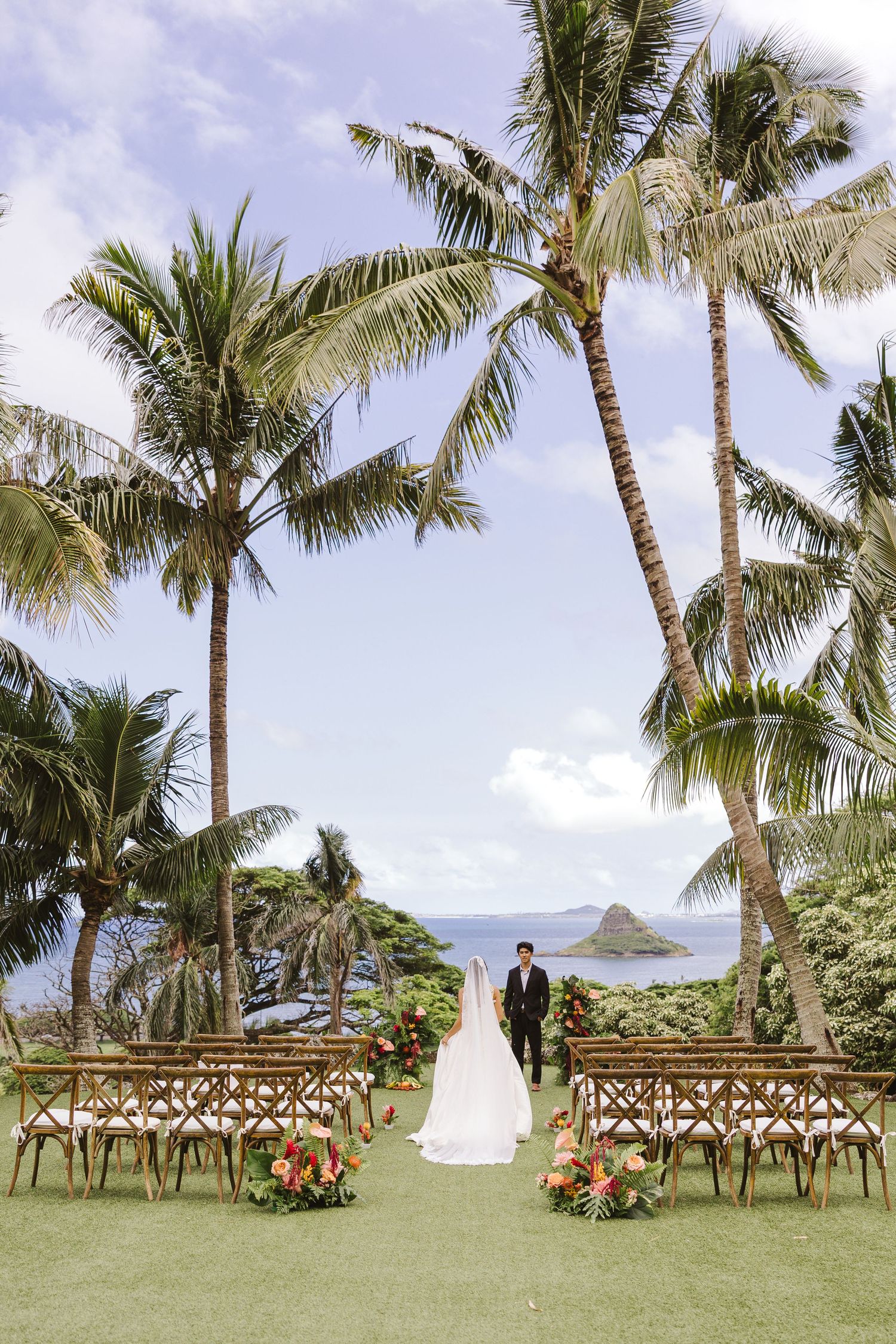Bride and groom walk down aisle at outdoor Hawaii wedding ceremony with palm trees and ocean views.