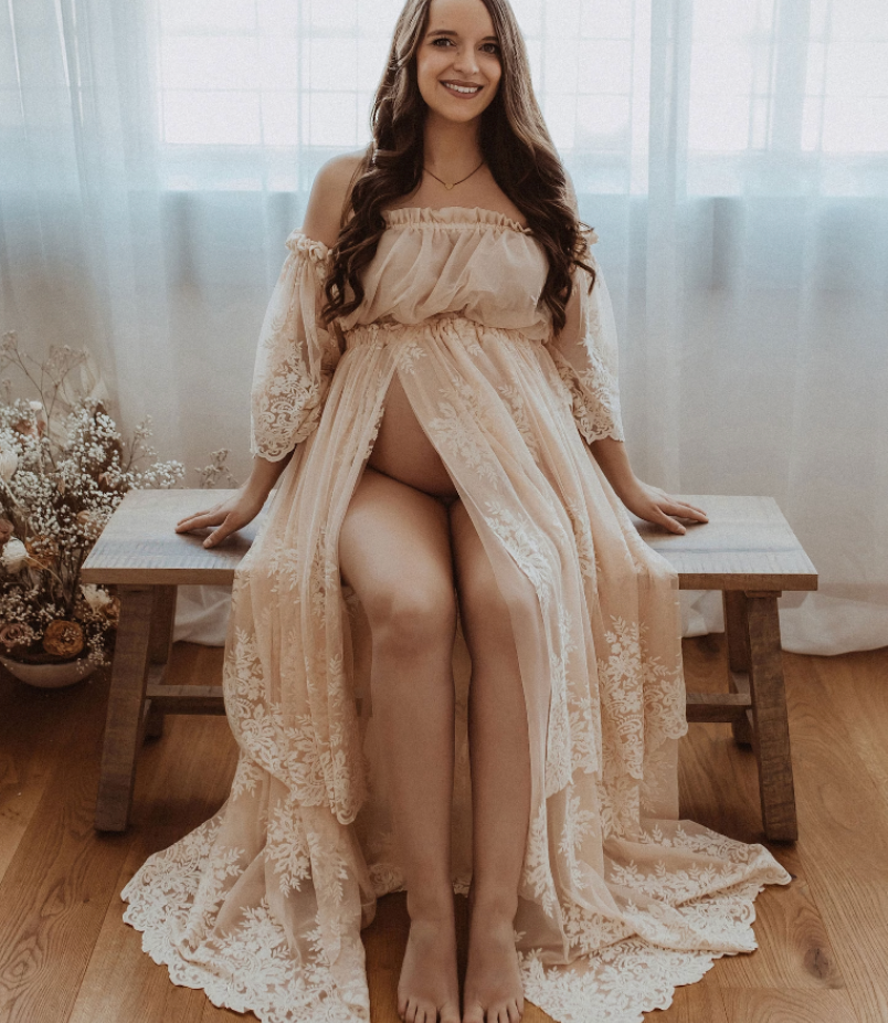 Delicate lace maternity boudoir photo featuring cream-colored dress on wooden bench.