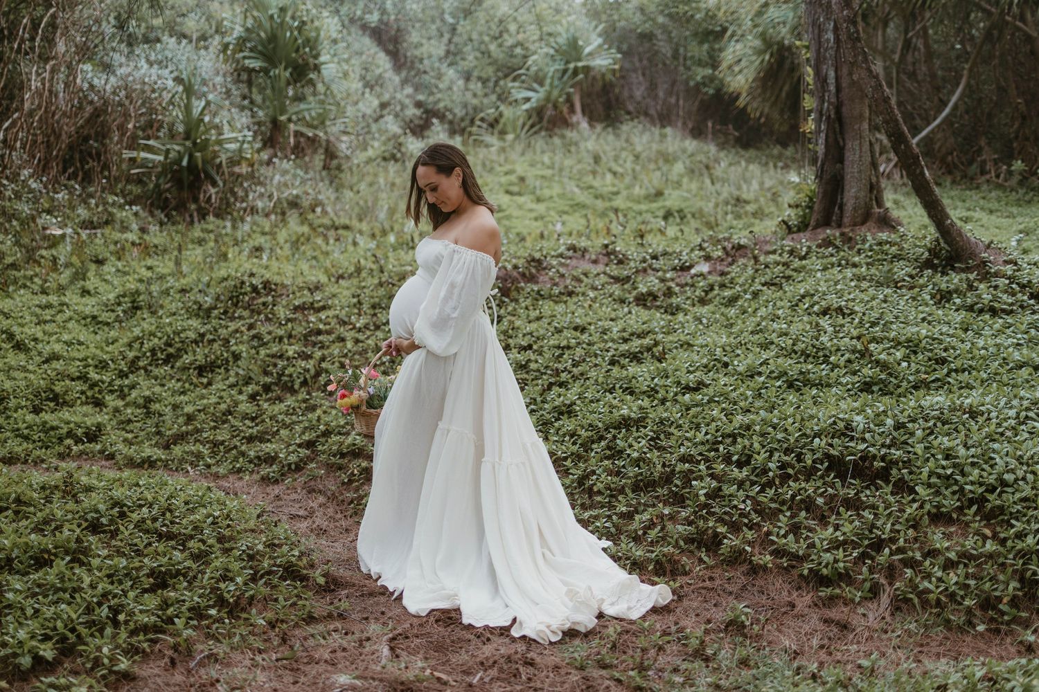 Ethereal white maternity gown flowing in a woodland setting during a dreamy outdoor photoshoot.