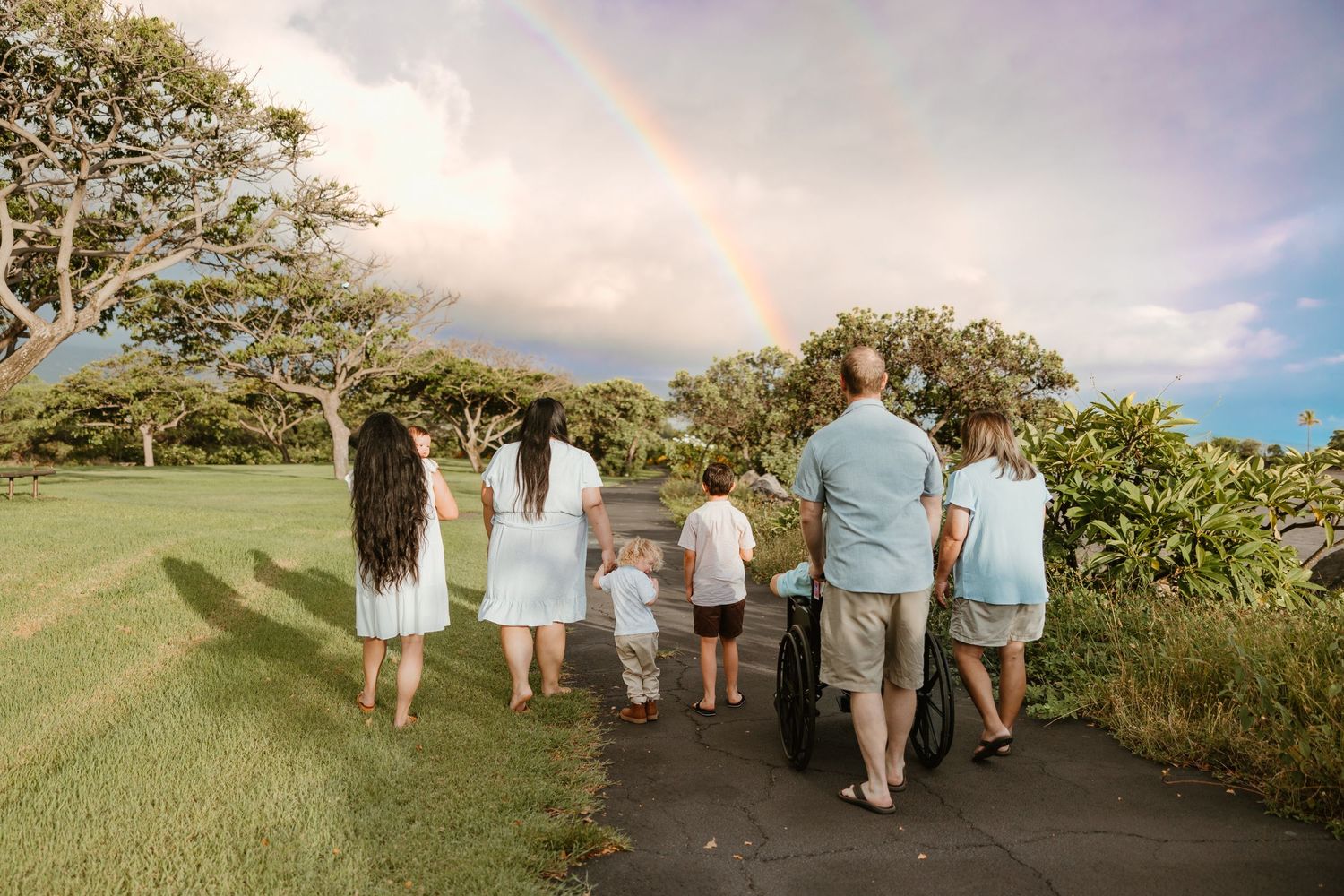 Family walking together on a path with a beautiful rainbow in the sky overhead.