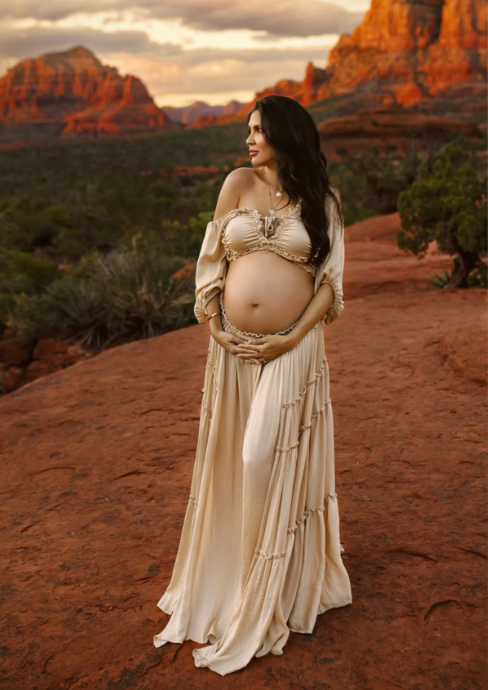 Maternity photoshoot in flowing cream dress against red rock formations at sunset.