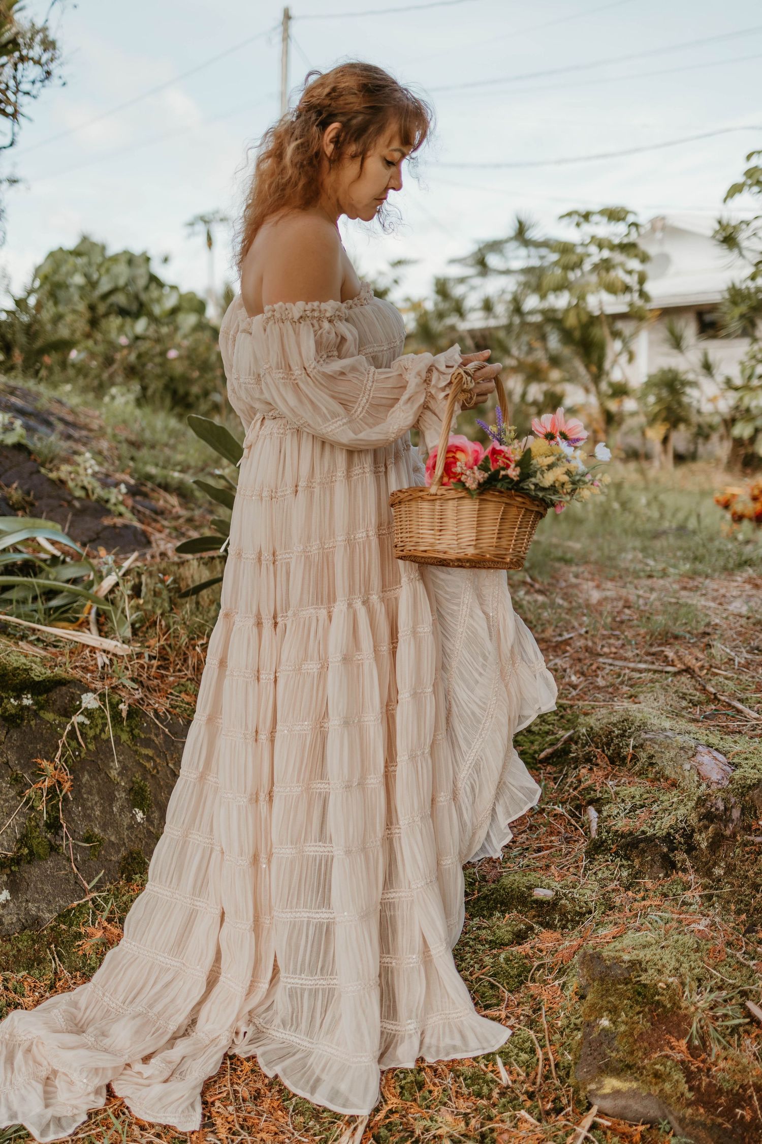 Romantic off-shoulder cream dress with basket of flowers in garden setting.