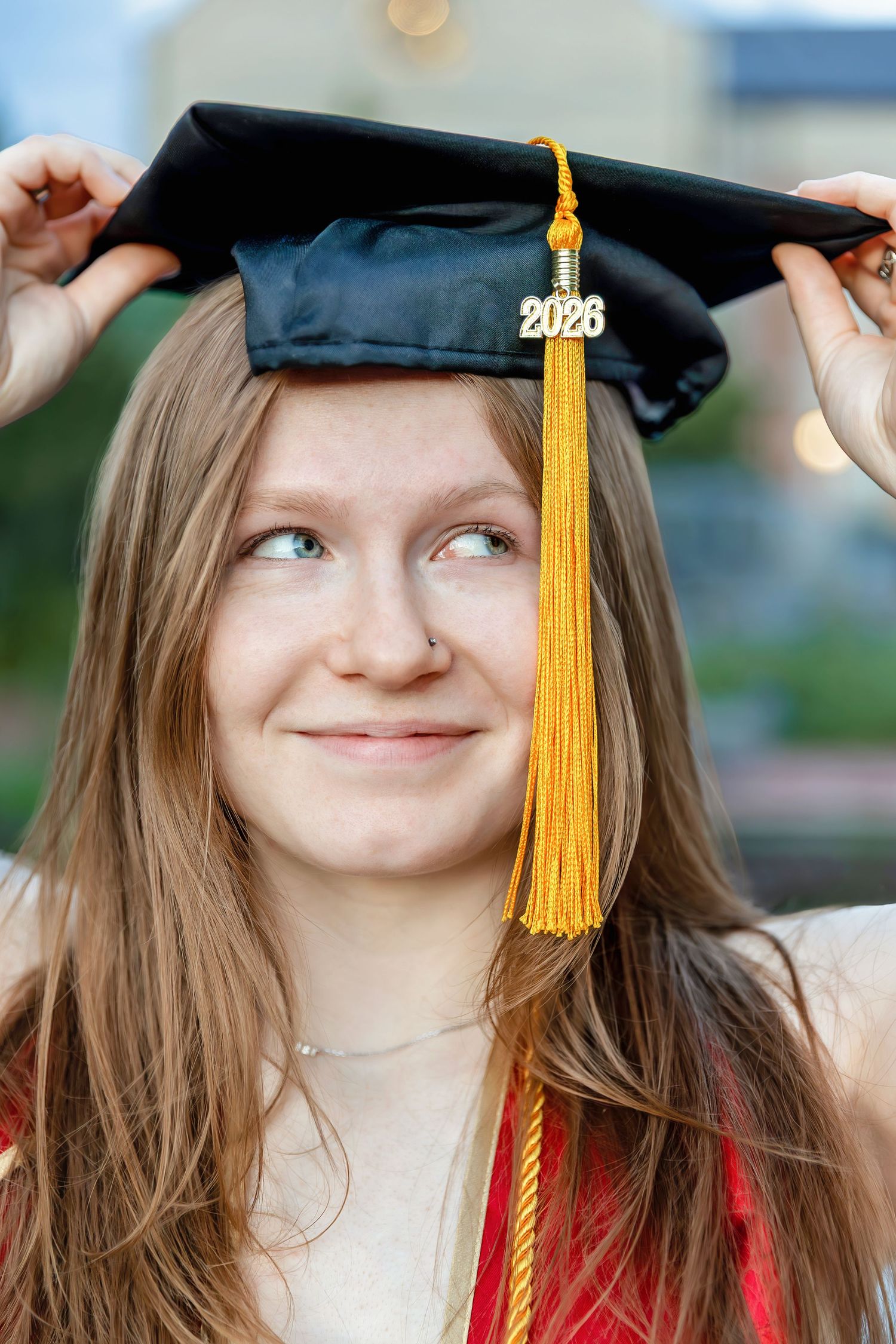 A young woman smiles while adjusting her 2026 graduation cap with a gold tassel.