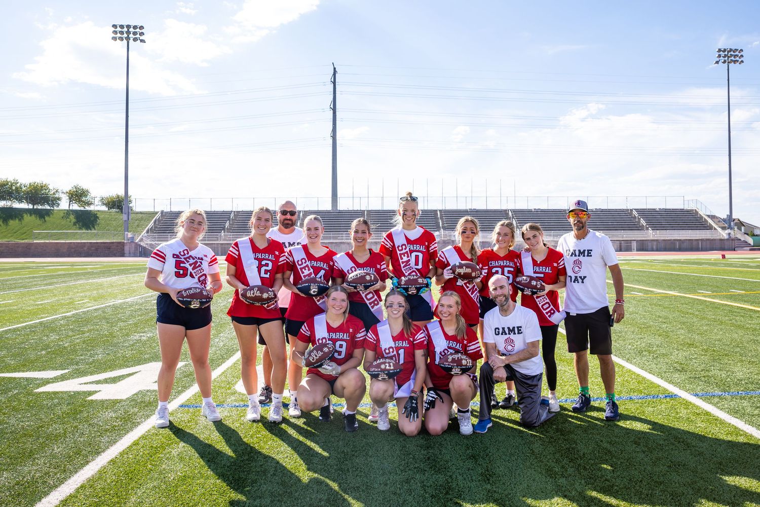A girls flag football team poses together on a turf field for a group photo.