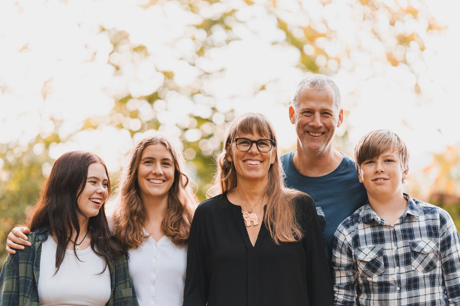 A cheerful family of five smiling together in an outdoor portrait.