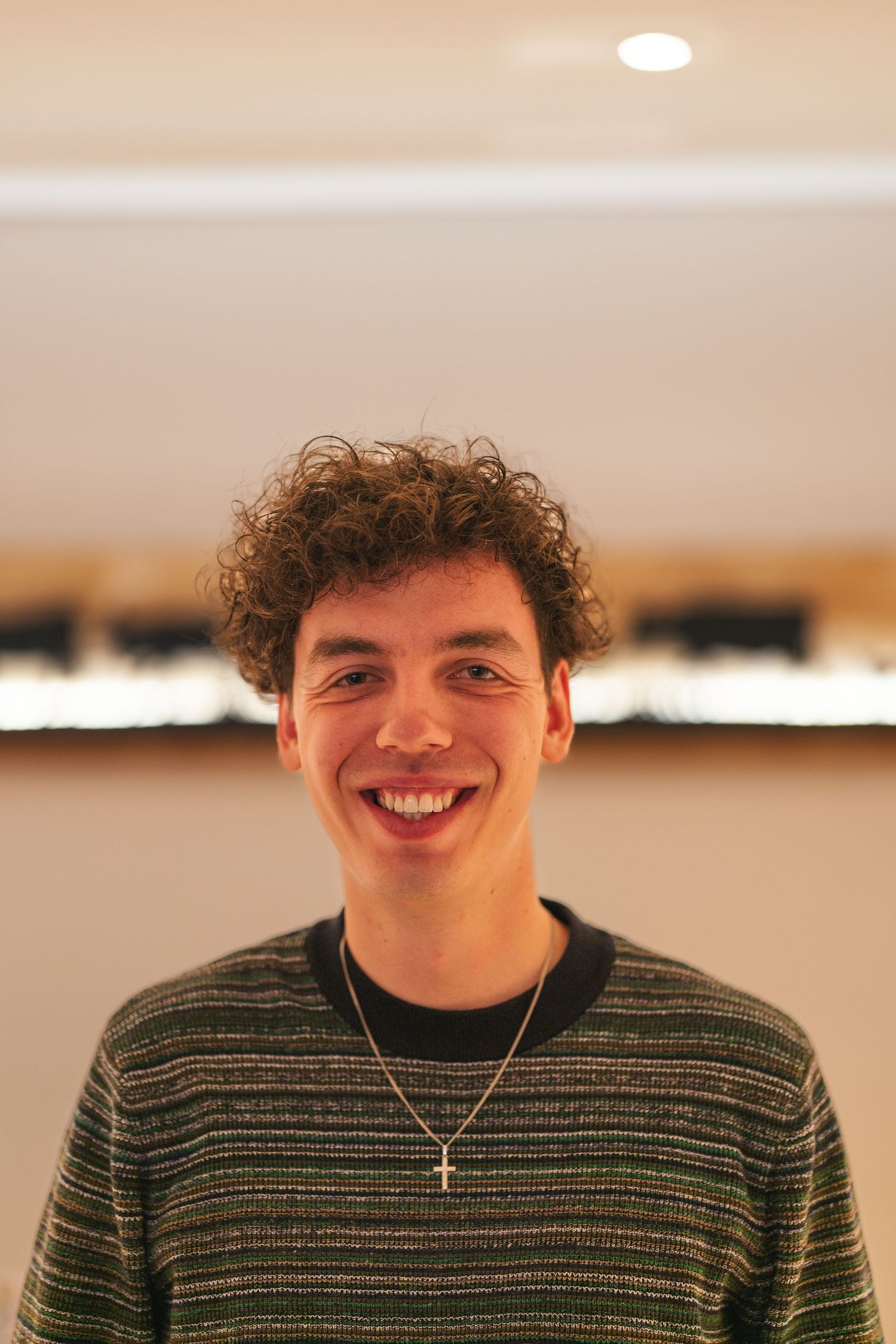 A candid portrait of someone in a striped sweater and cross necklace with curly hair.