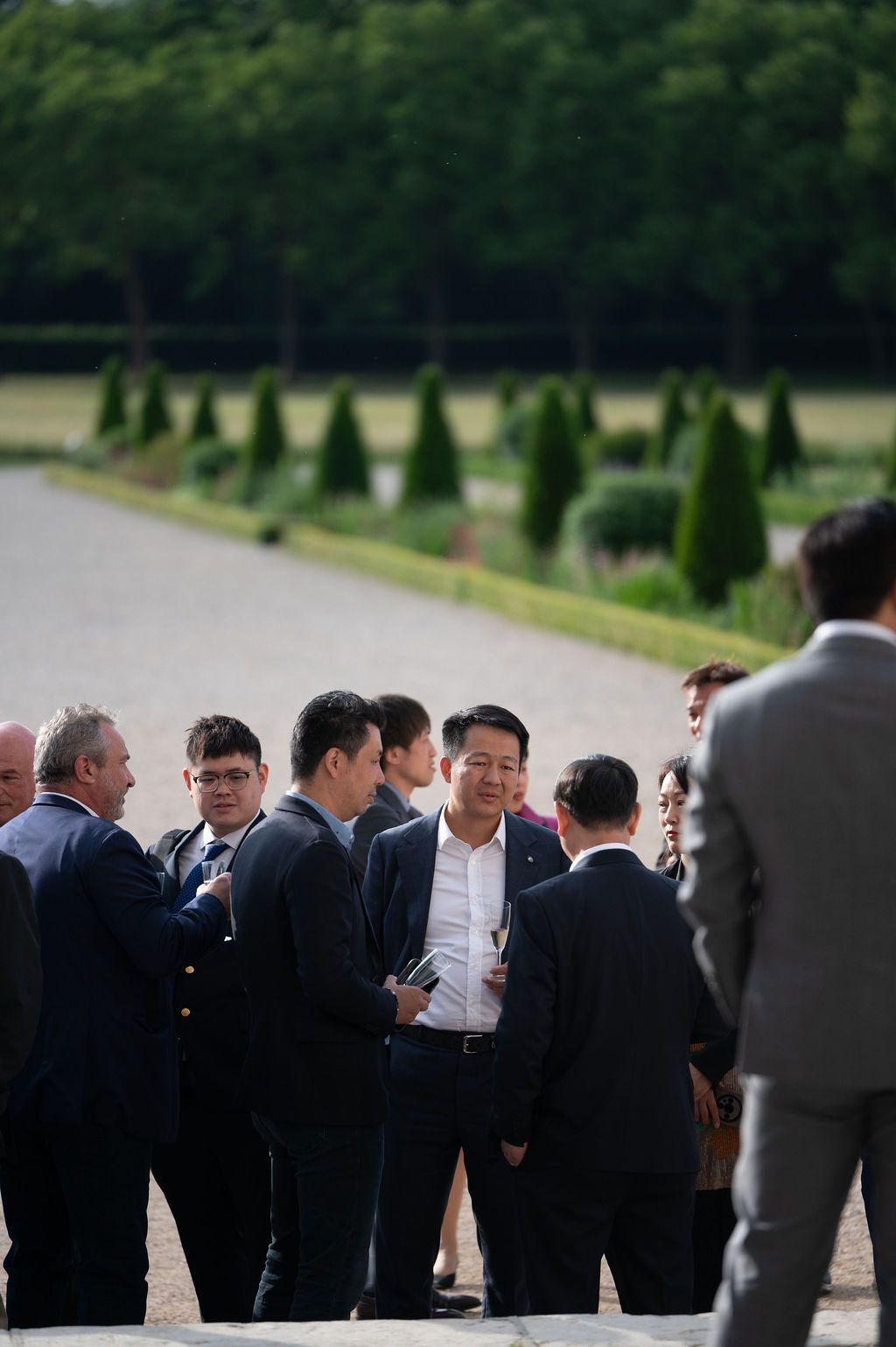 Cadre debout pour un networking spontané, jardins à la française du Château de Chambord en fond.