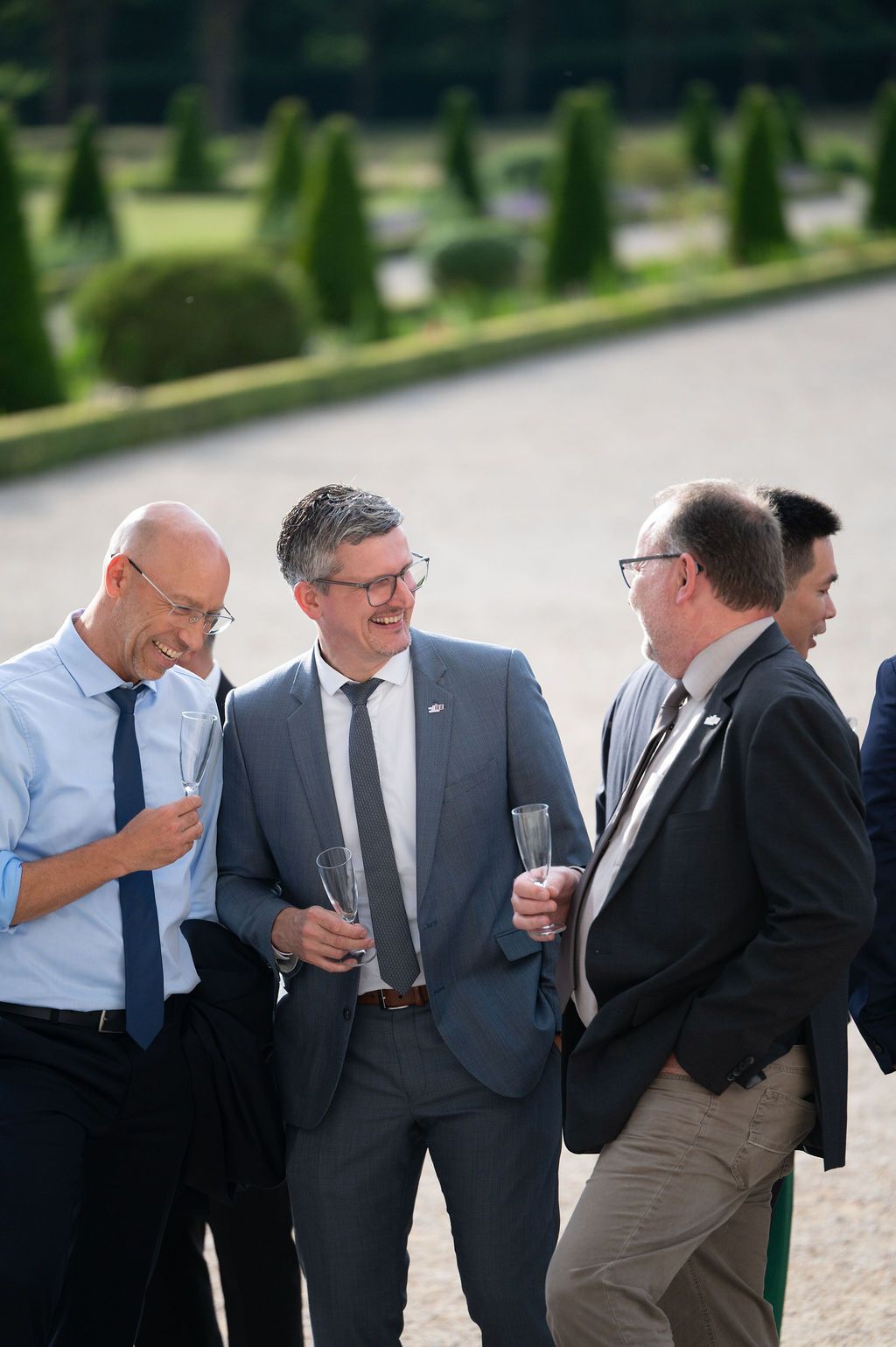 Trio de dirigeants debout, verres de champagne en main, échange autour d’un projet.