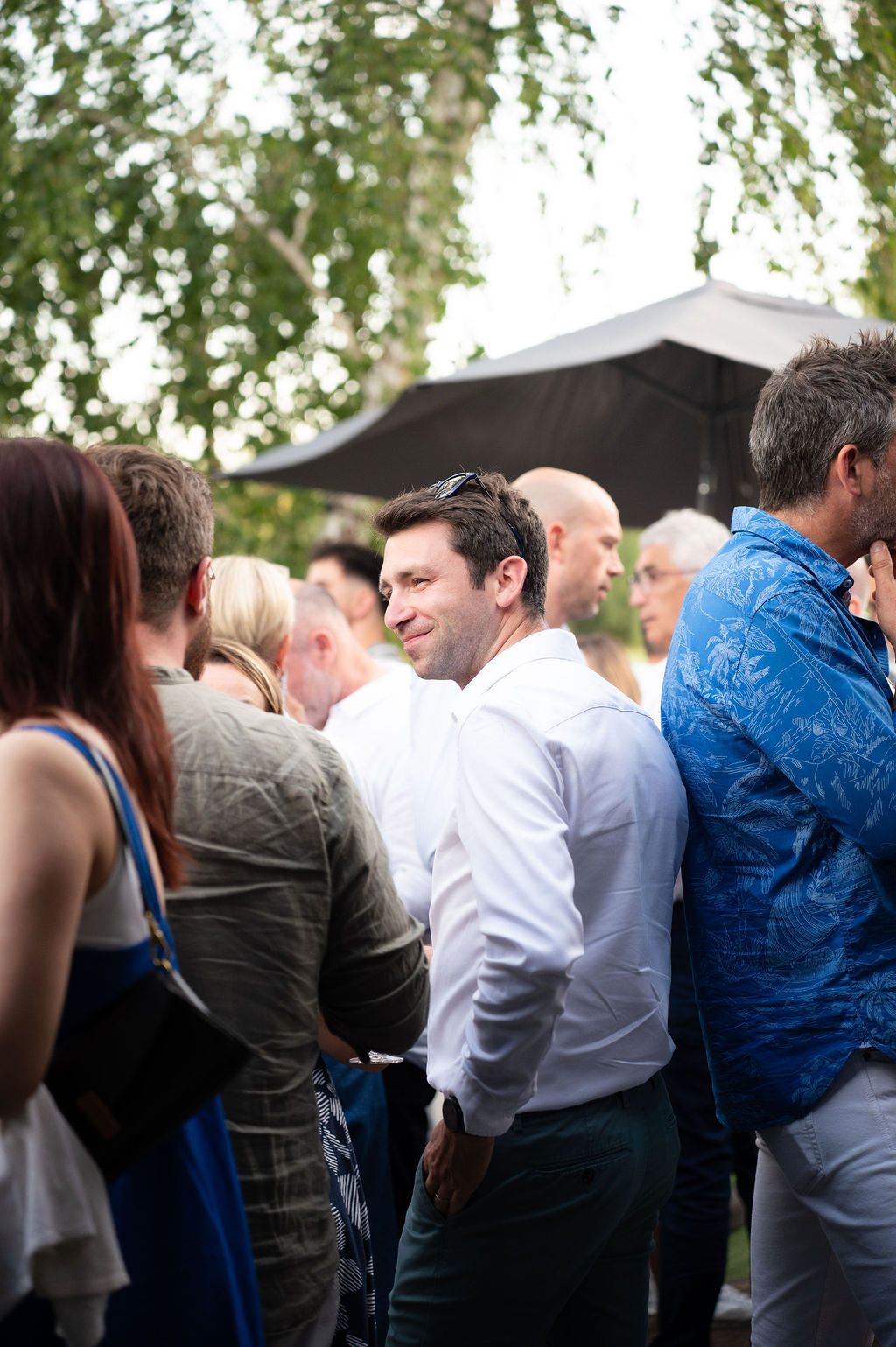 Dirigeants réunis lors d’un cocktail en extérieur, échanges conviviaux à l’ombre des arbres en soirée.