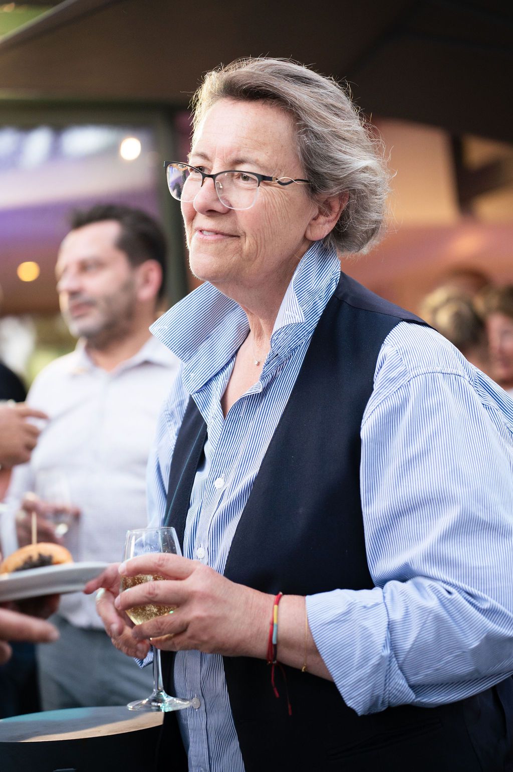 Portrait d’une participante à l’événement, verre de vin à la main, ambiance conviviale au cocktail de fin de journée