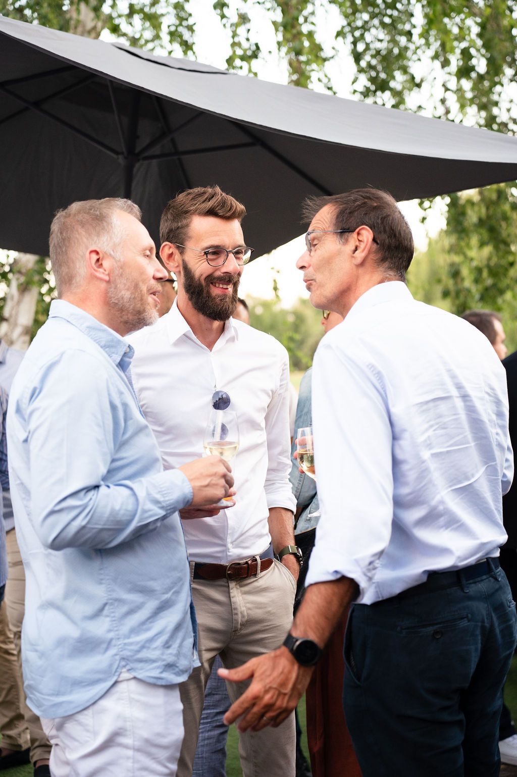 Trois chefs d’entreprise discutent avec le sourire, verre à la main, ambiance détendue en terrasse.