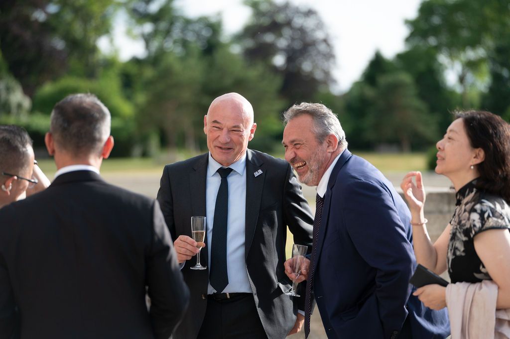 Dirigeants en costume échangeant sourires et champagne sur la terrasse du Château de Chambord, jardins en arrière‑plan.