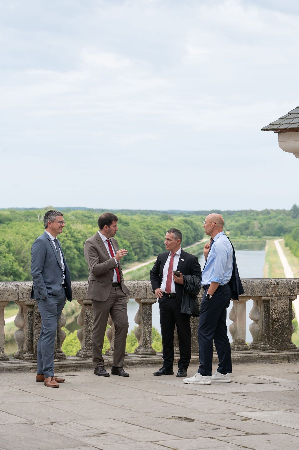 Quatre dirigeants en costume debout sur la terrasse, ambiance corporate au château.