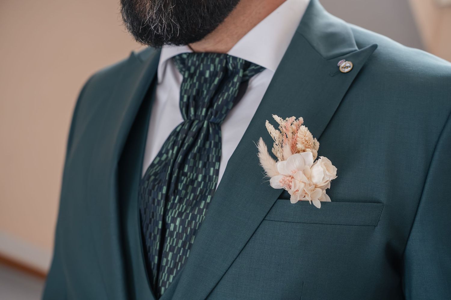 Groom in a dark green suit with a patterned green tie and a dried flower boutonniere pinned to the breast pocket.