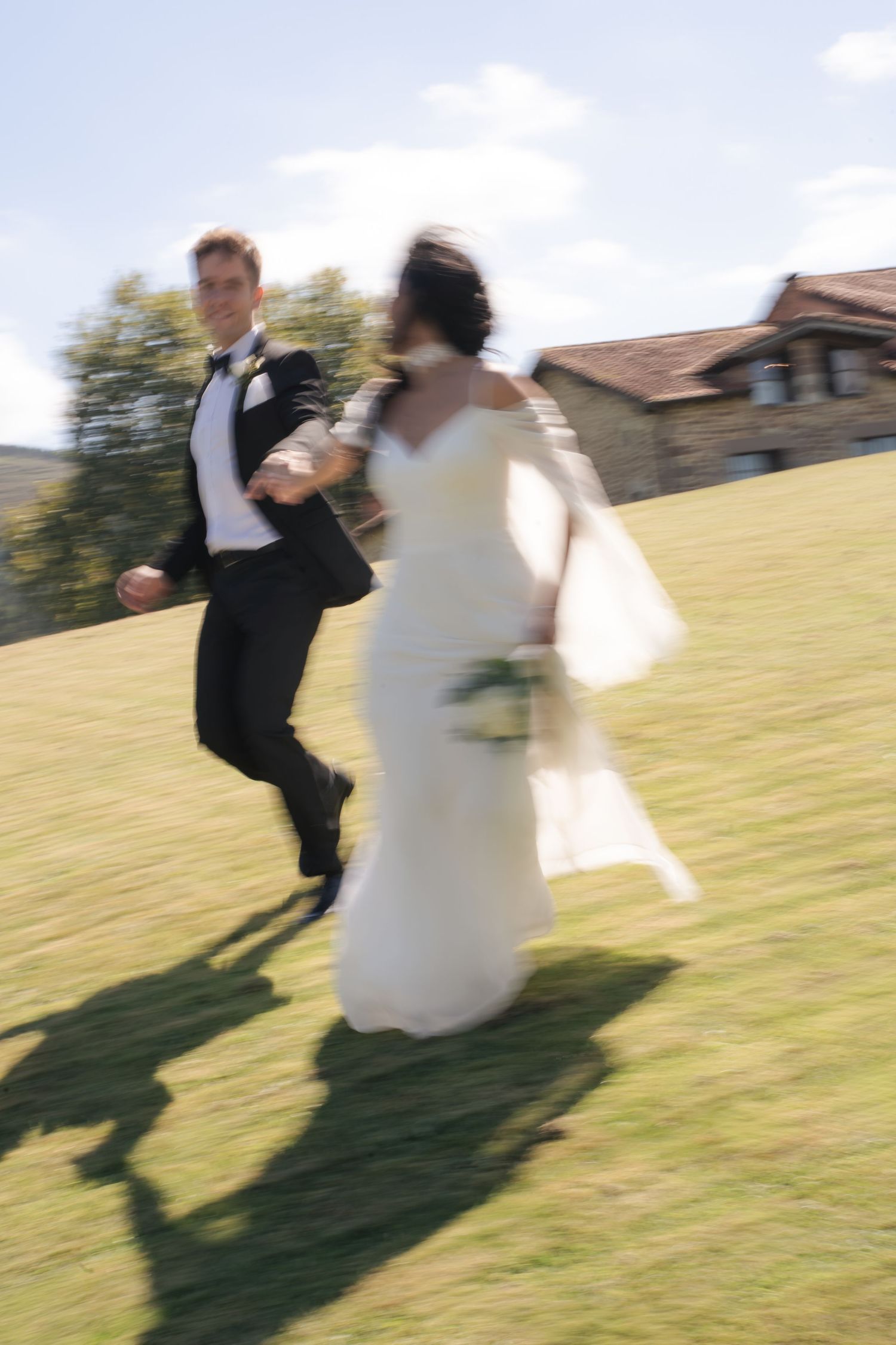 Joyful bride and groom running hand-in-hand across green lawn on sunny wedding day.