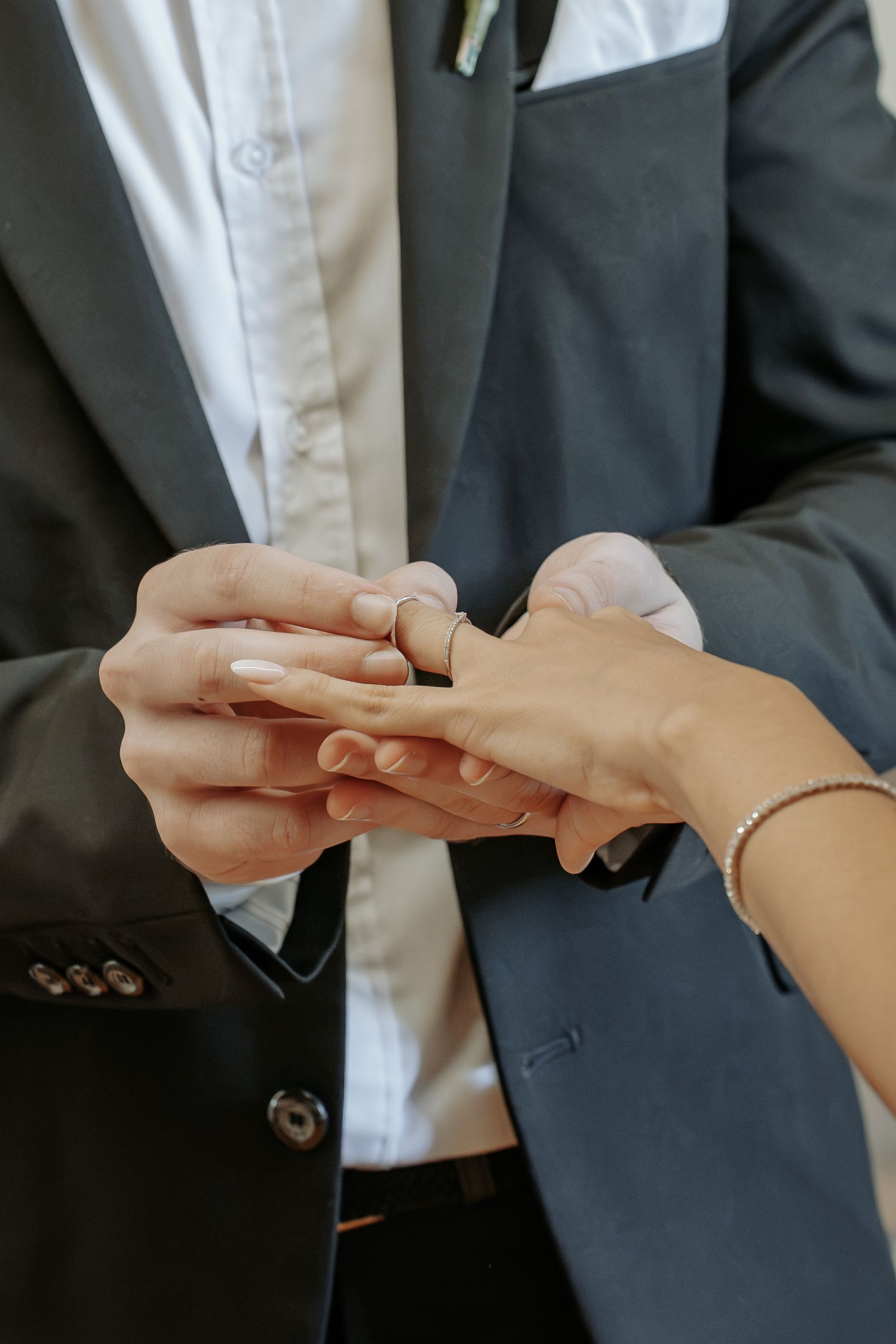 Groom placing a wedding ring on bride's finger during ceremony, close-up of hands with bracelet.