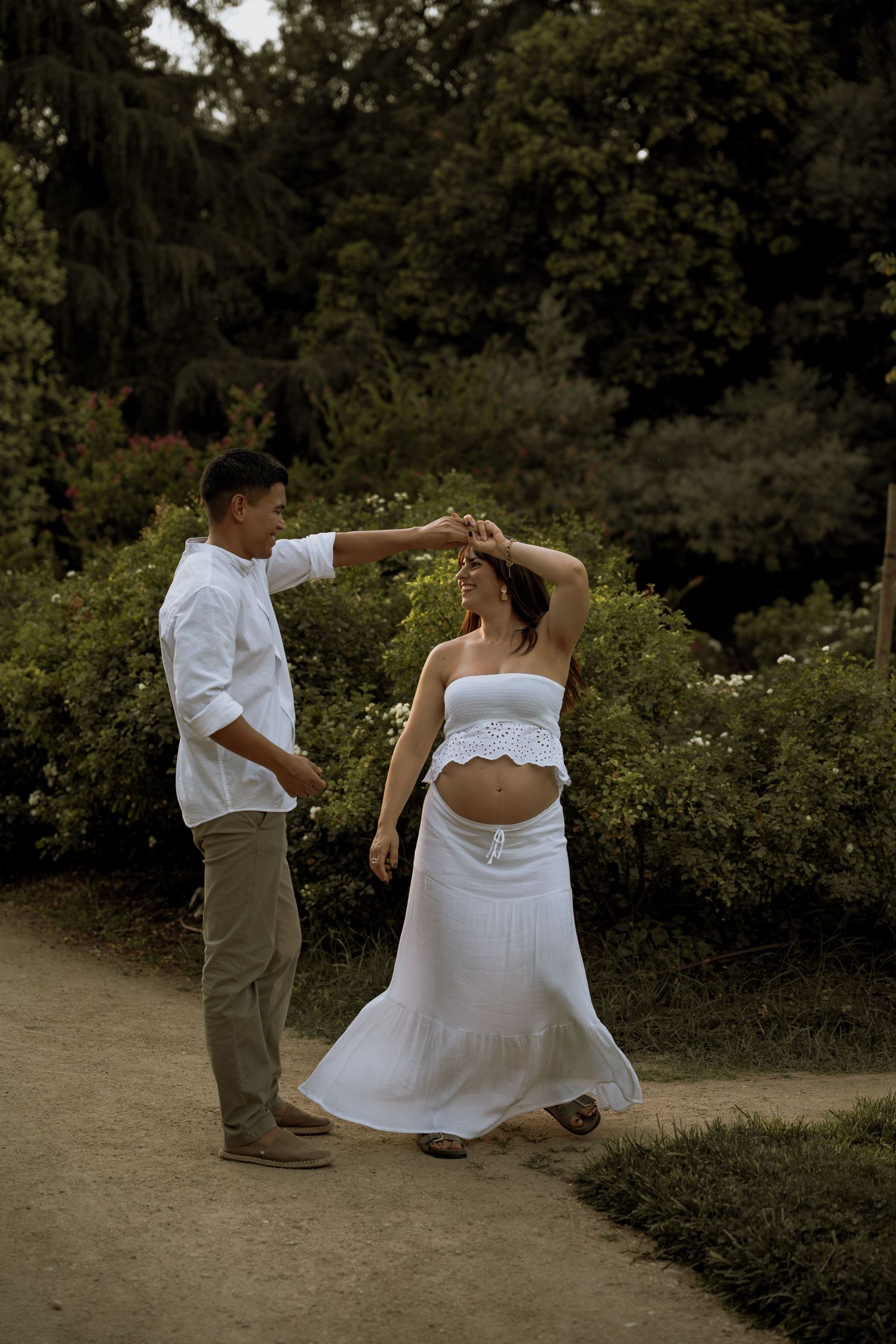 Expecting couple dancing together on a garden path during an outdoor maternity photoshoot.