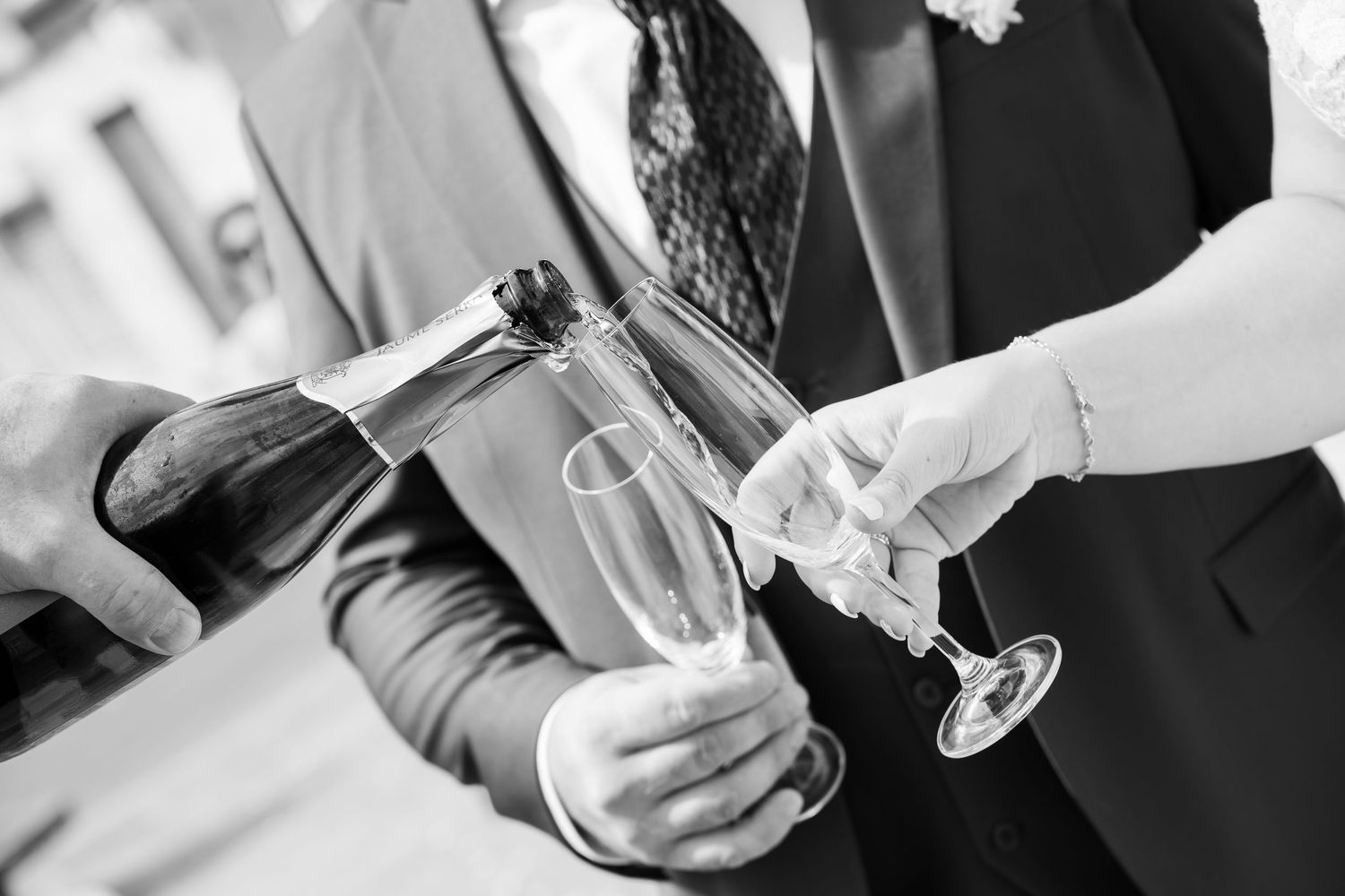 Black and white photo of champagne being poured into flutes at a formal wedding celebration.