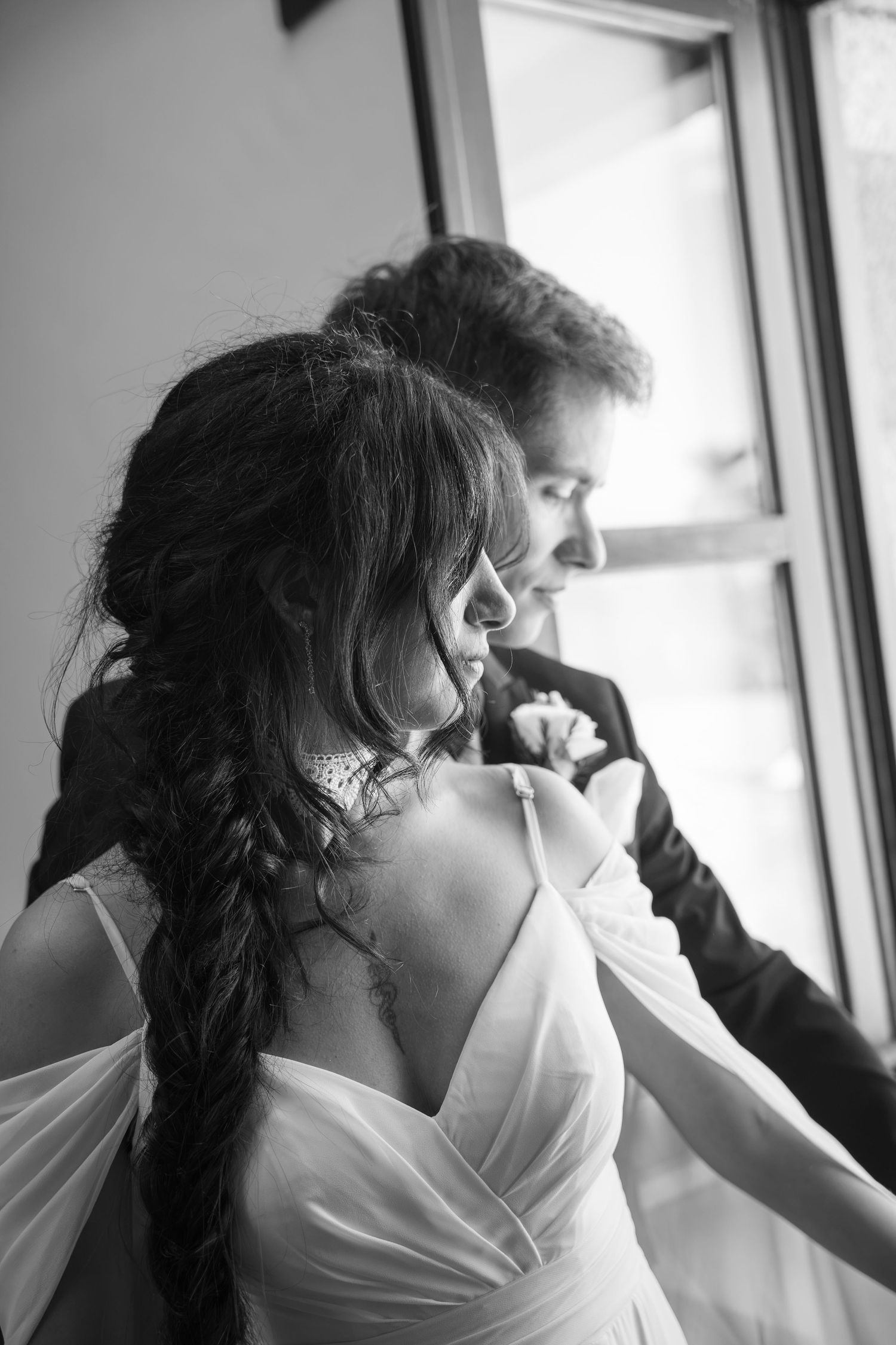 Black and white photo of a bride and groom sharing an intimate moment by a window on their wedding day.