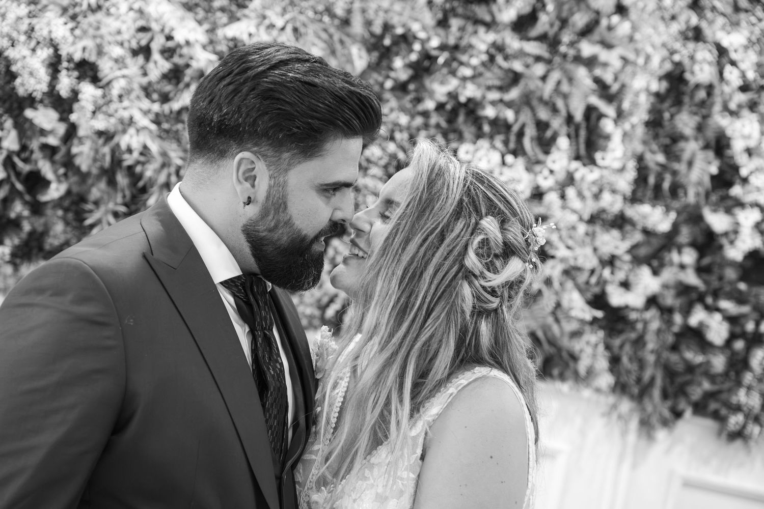 Black and white photo of a couple sharing an intimate moment at their wedding, surrounded by a floral backdrop.