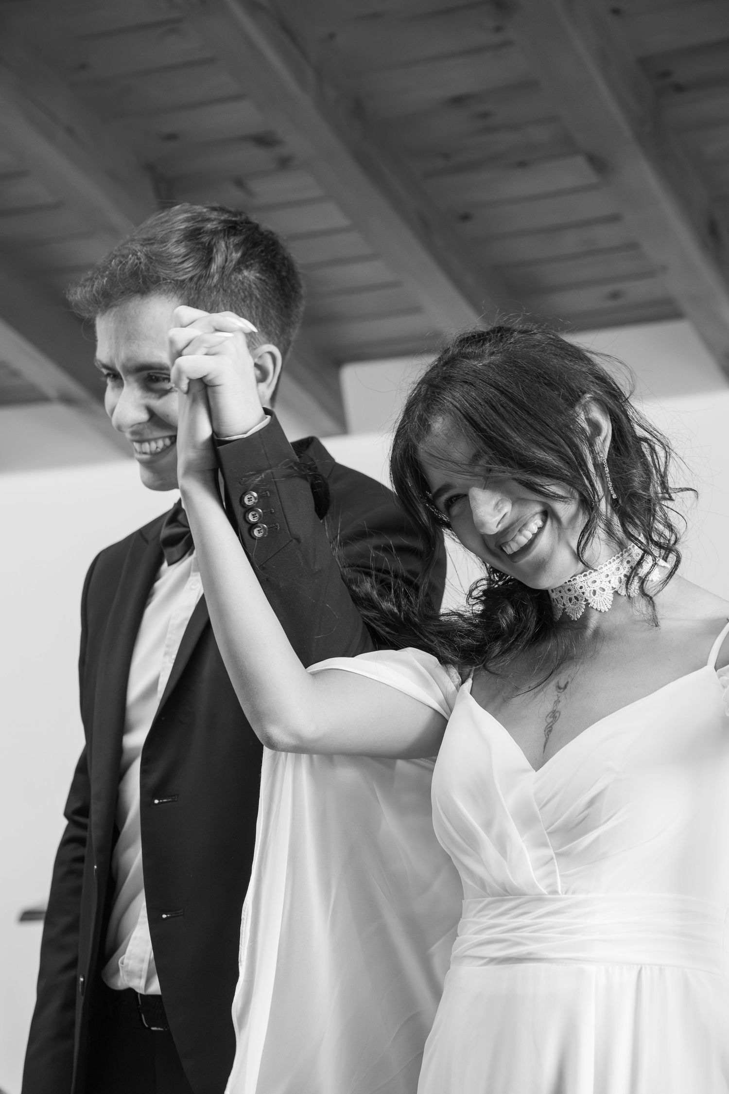 Black and white photo of a joyful bride and groom dancing and laughing together on their wedding day.
