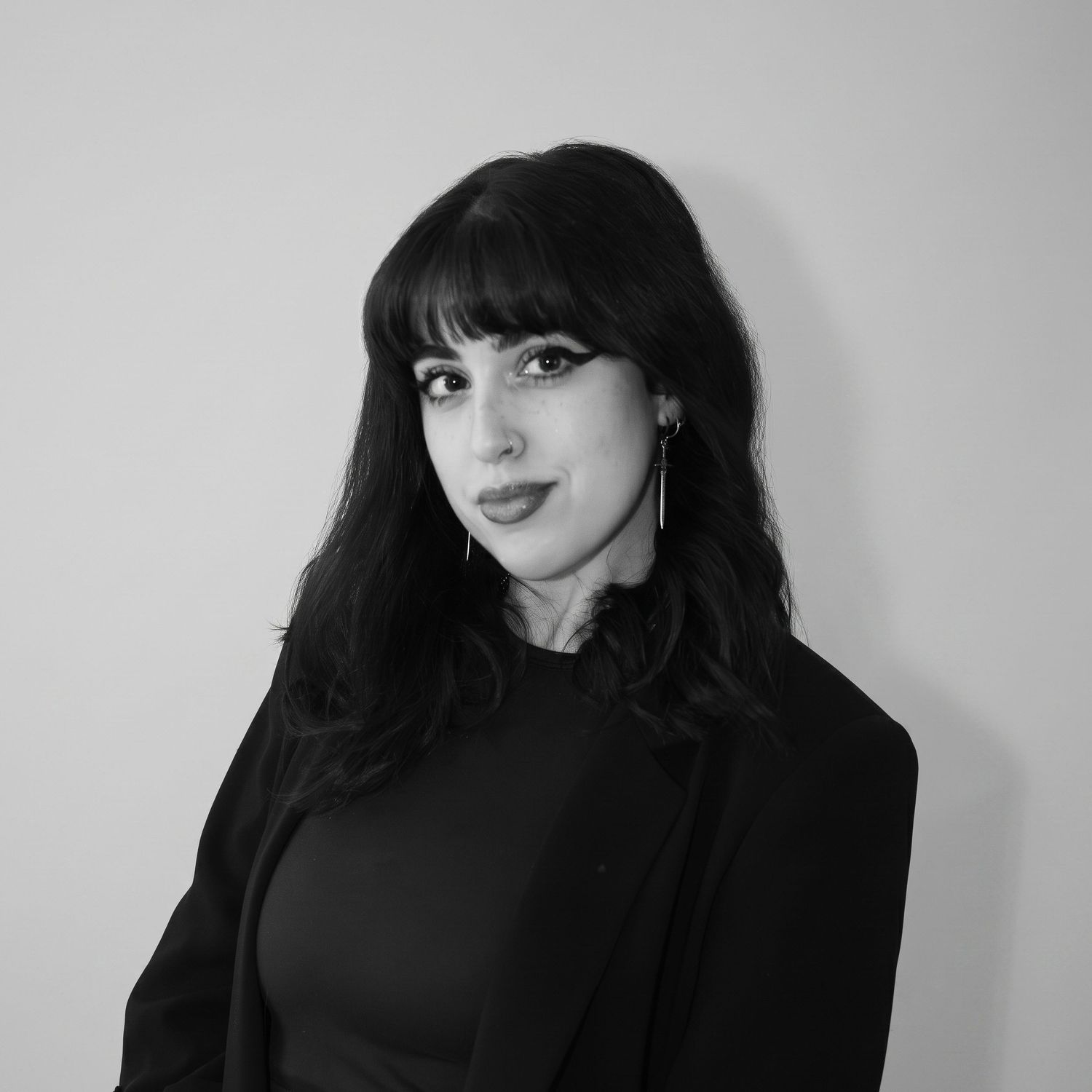 Elegant black and white photo of a dark-haired woman with bangs in a black blazer posing confidently.