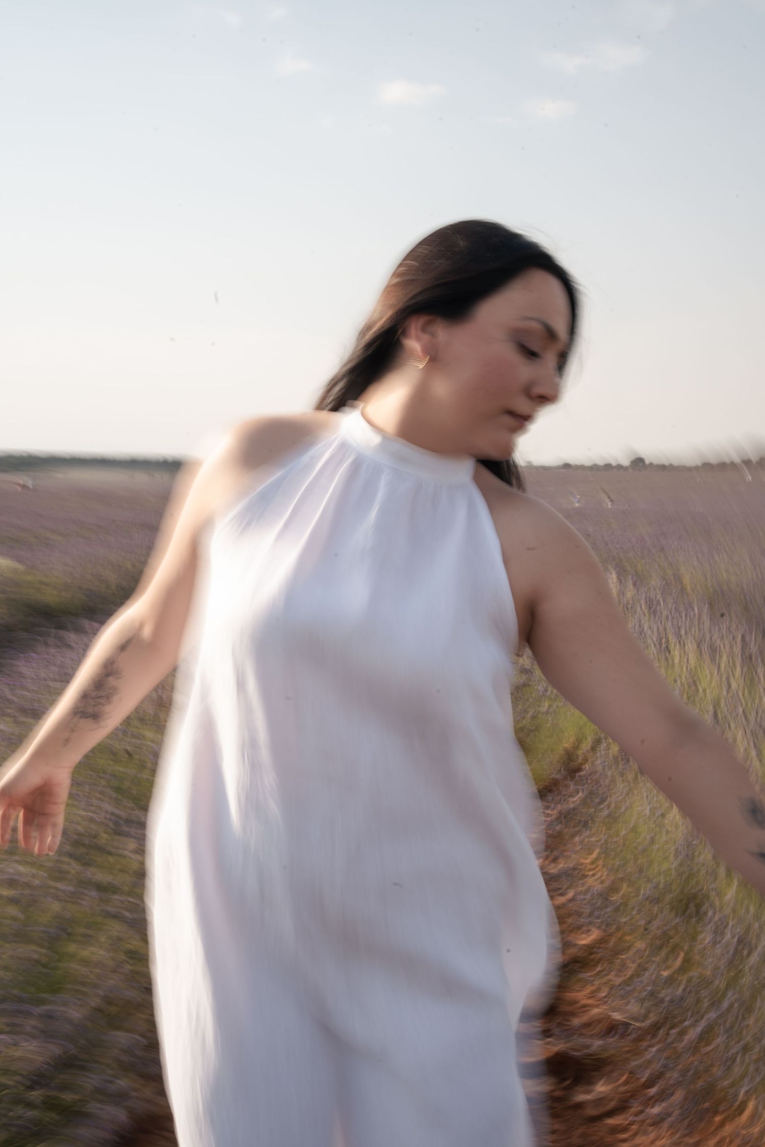 Woman in white halter dress spinning in a lavender field at golden hour.