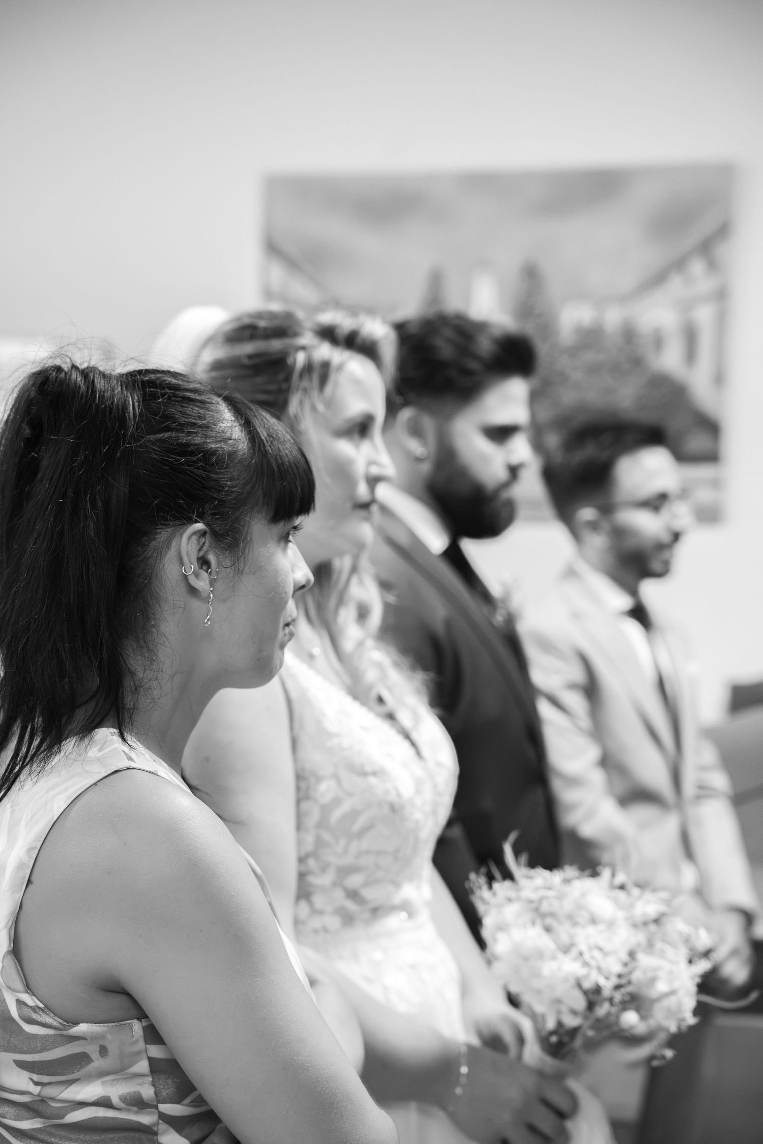 Black and white photo of a bride holding a bouquet standing beside wedding guests during a ceremony in a church.