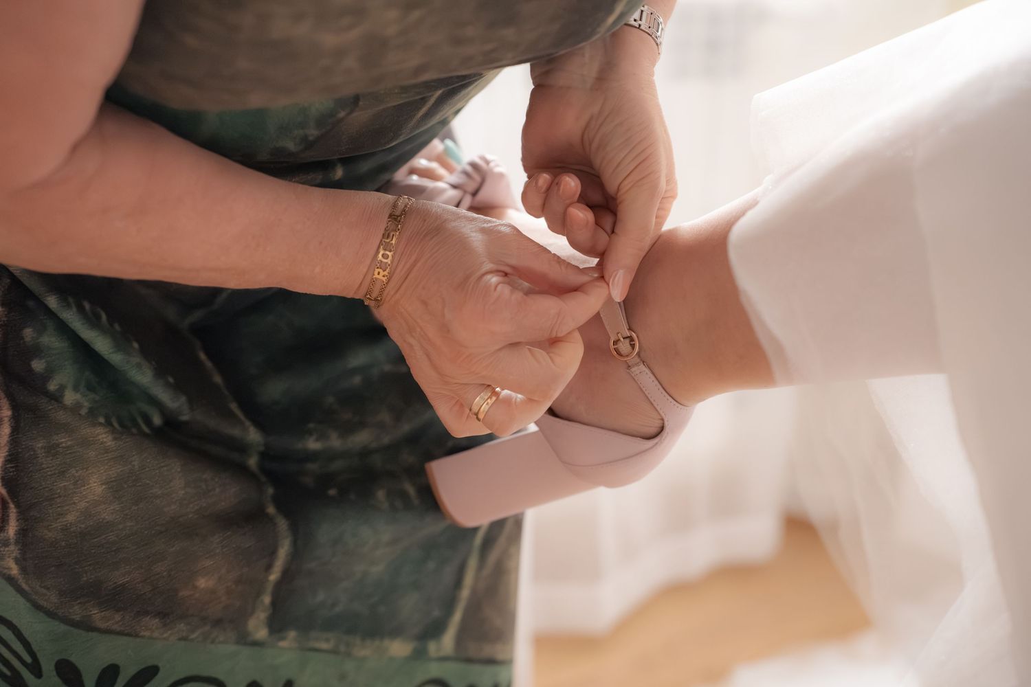Close-up of hands fastening a delicate bracelet on a bride's wrist during wedding preparations.