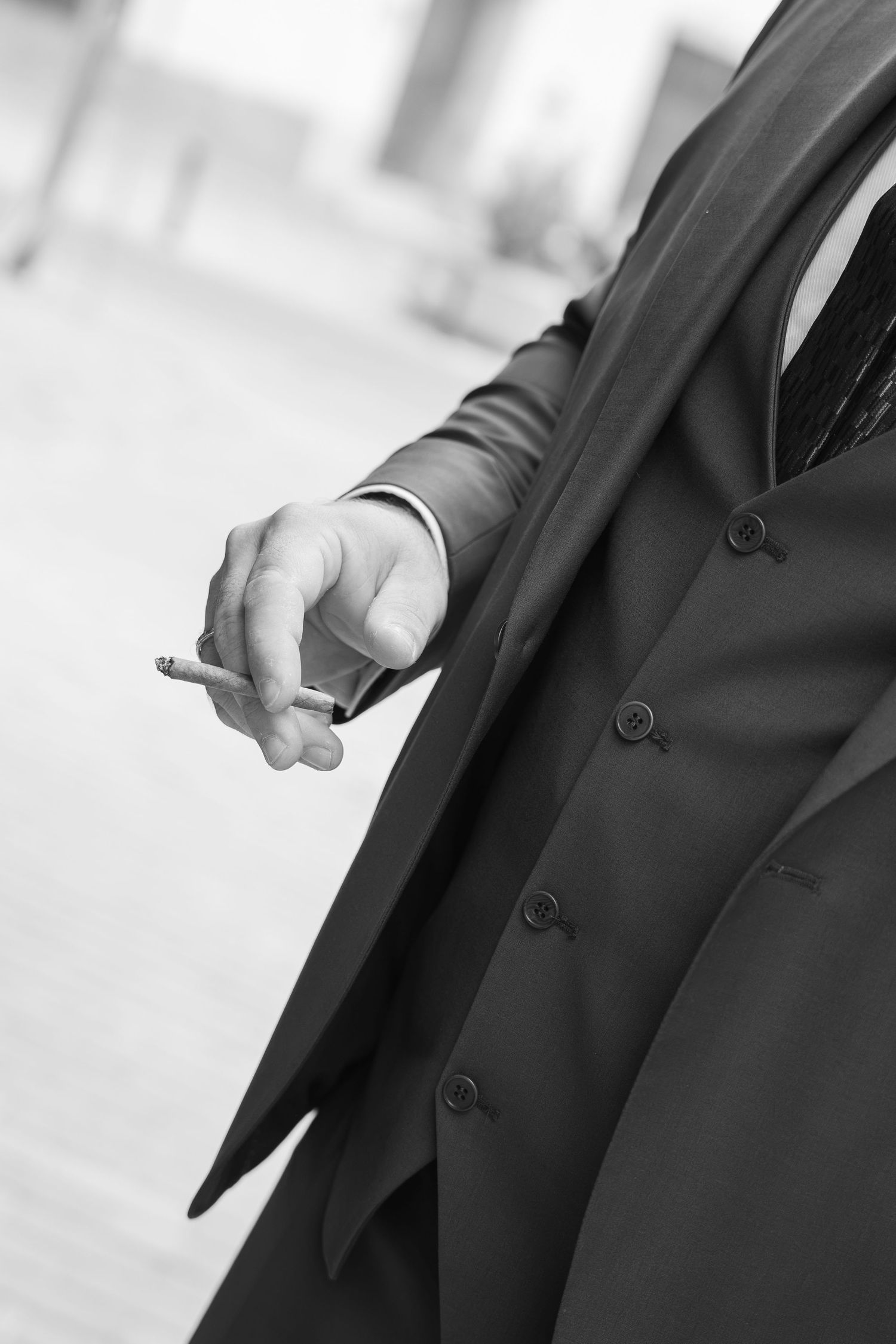 Black and white photo of a man in a suit holding a cigarette outdoors.