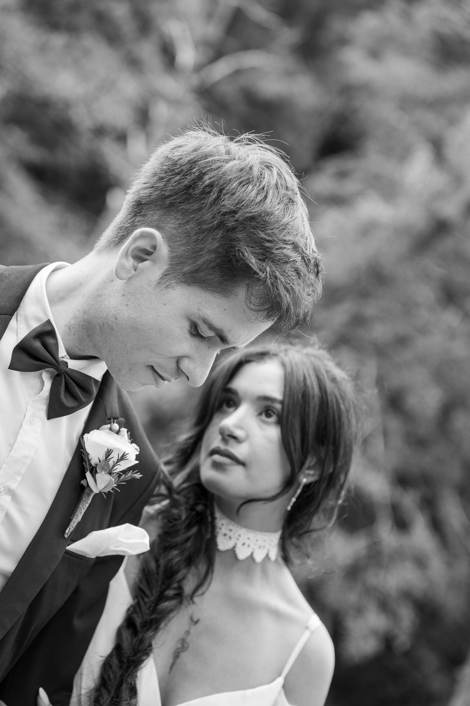 Black and white wedding portrait of a groom in a bow tie and boutonniere gazing down as a bride with a braid looks up at him.