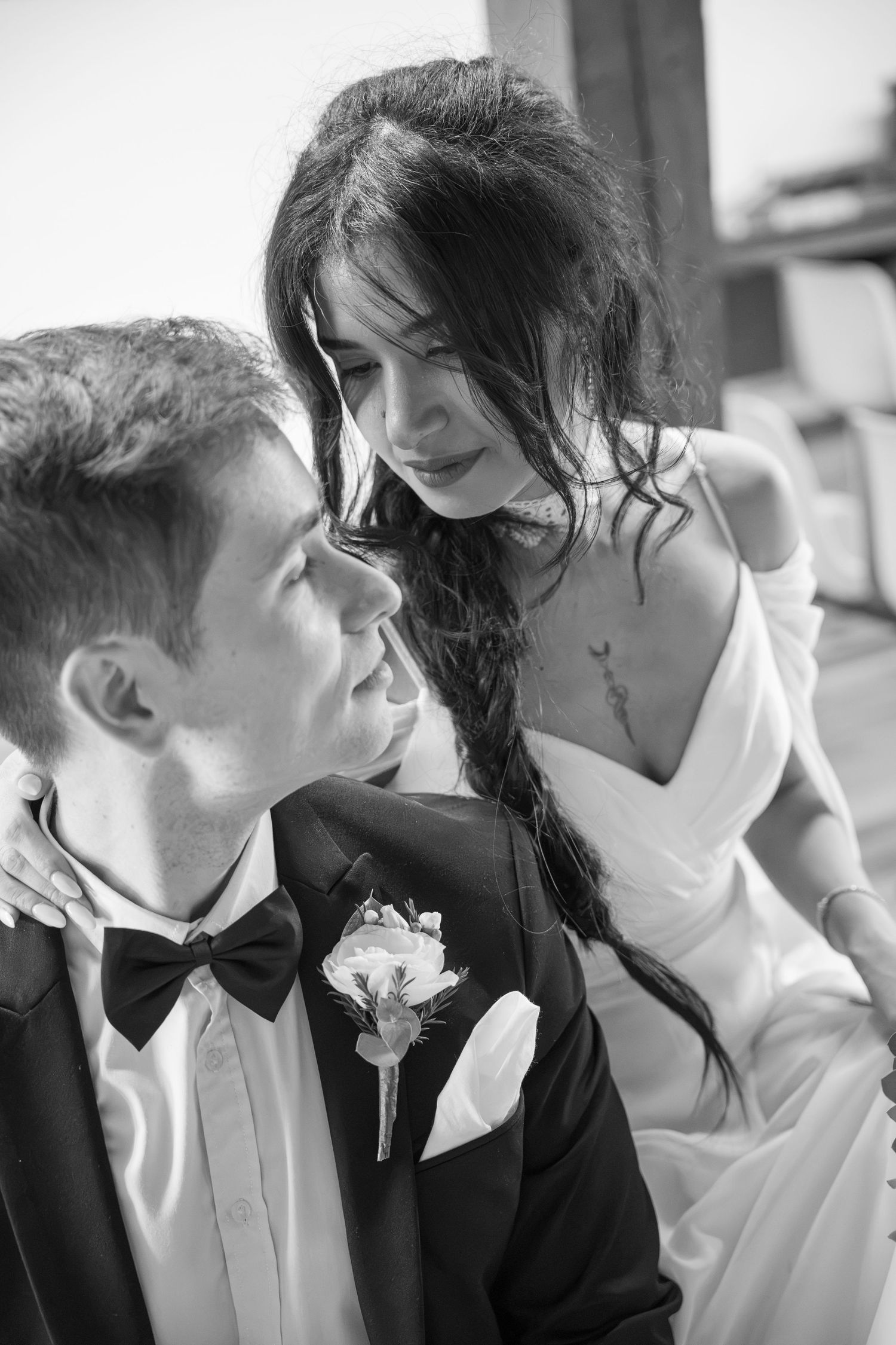 Black and white wedding portrait of a bride in a white gown leaning tenderly toward a groom in a tuxedo with a bow tie and boutonniere.