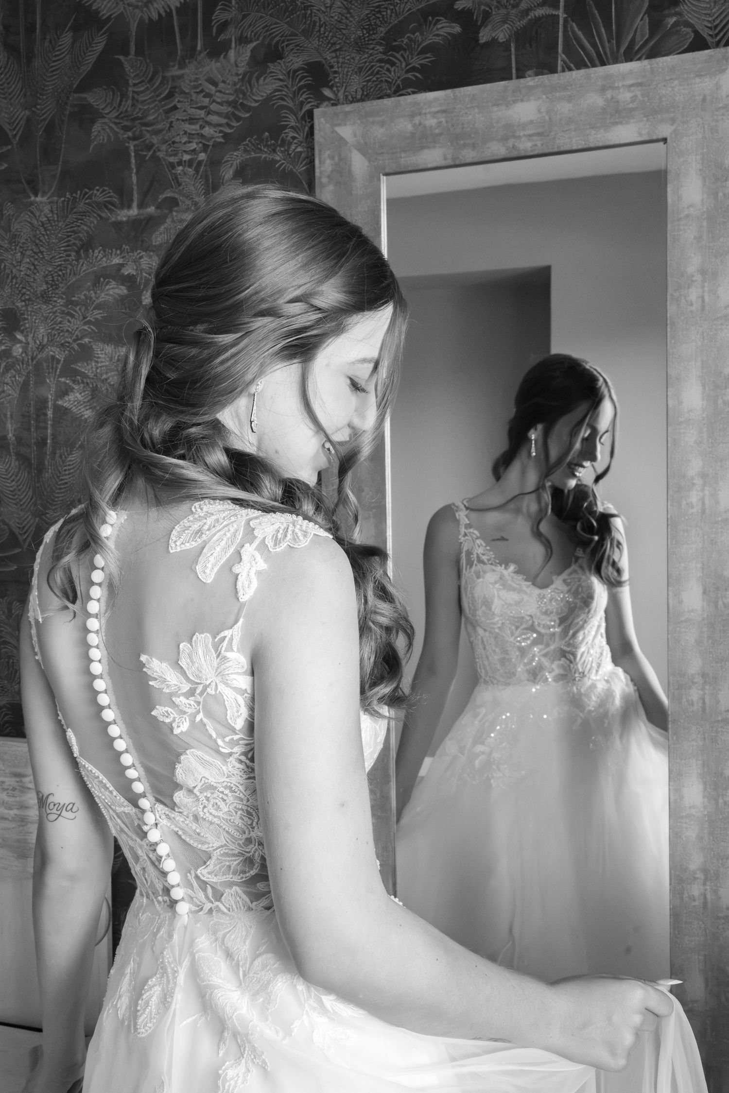 Black and white photo of a bride in a lace wedding dress with pearl buttons, reflected in a mirror.