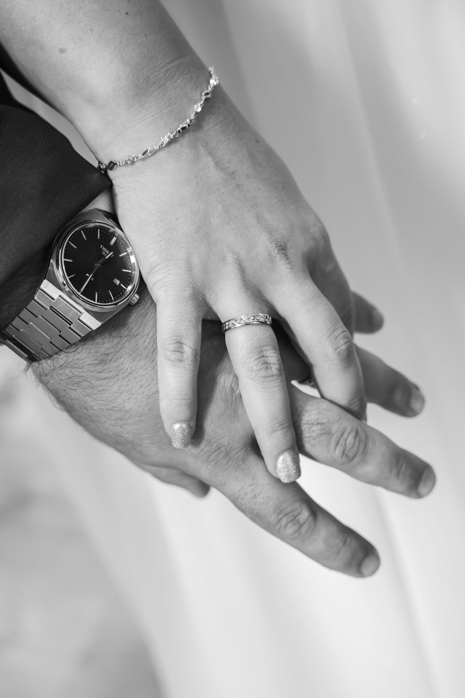 Black and white photo of newlyweds hands showing wedding rings, a diamond bracelet, and a classic Rolex watch.