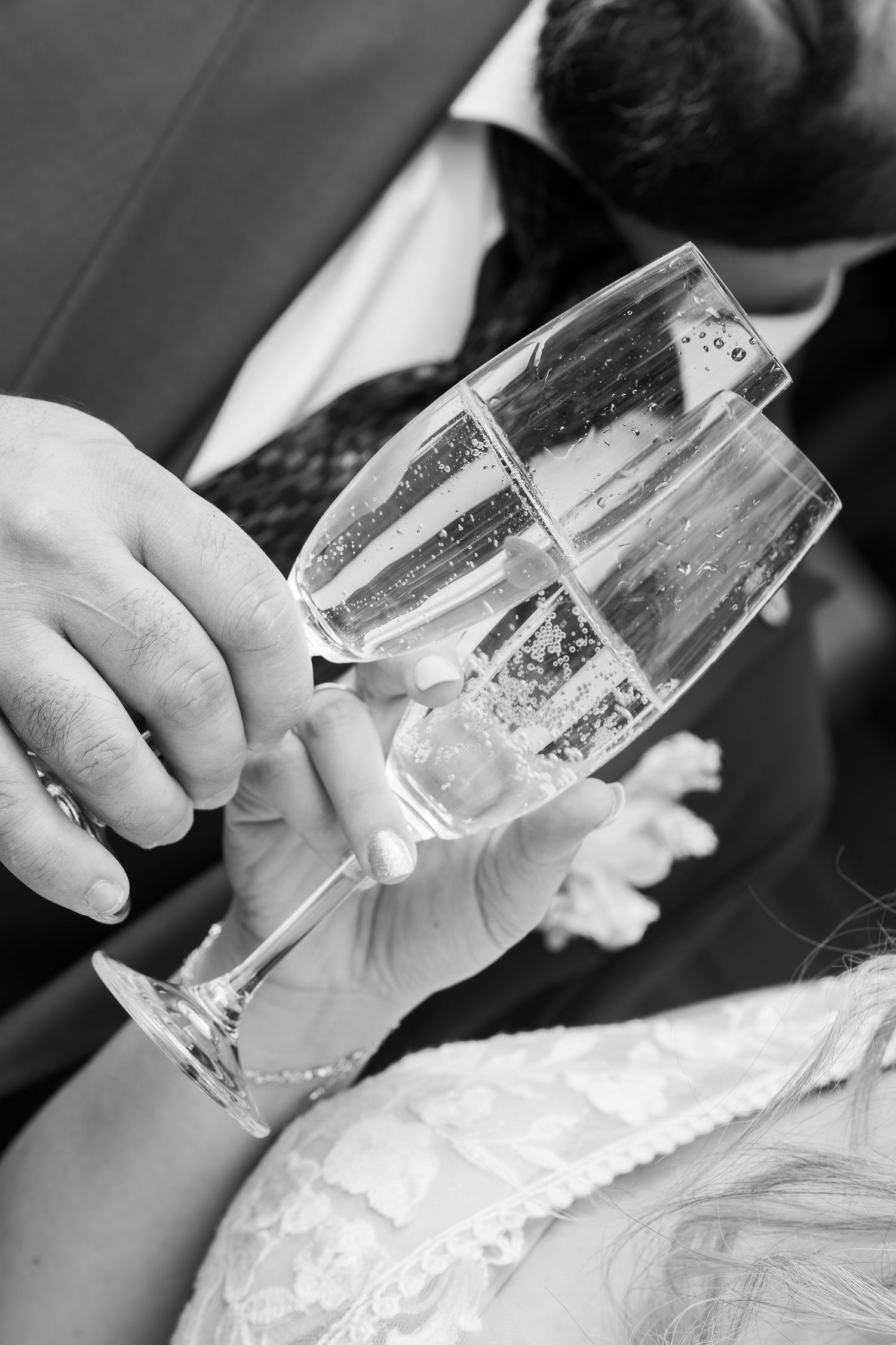 Black and white photo of bride and groom clinking champagne glasses at wedding reception.