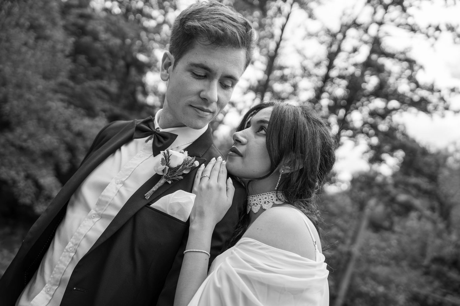 Black and white portrait of a couple embracing outdoors, the man in a vest and bow tie, the woman in a lace choker and shawl.