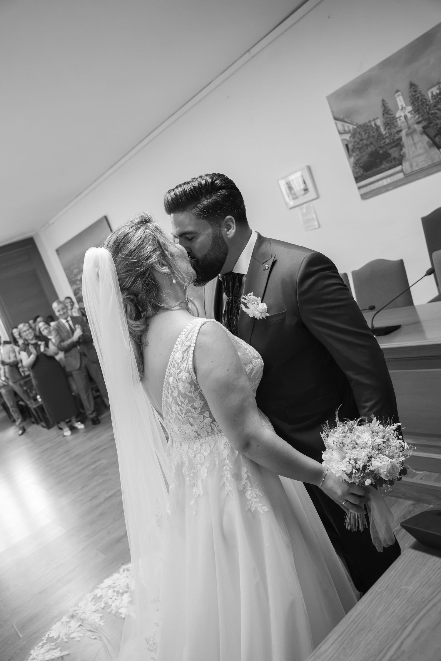 Black and white photo of a bride and groom sharing their first kiss at a wedding ceremony.
