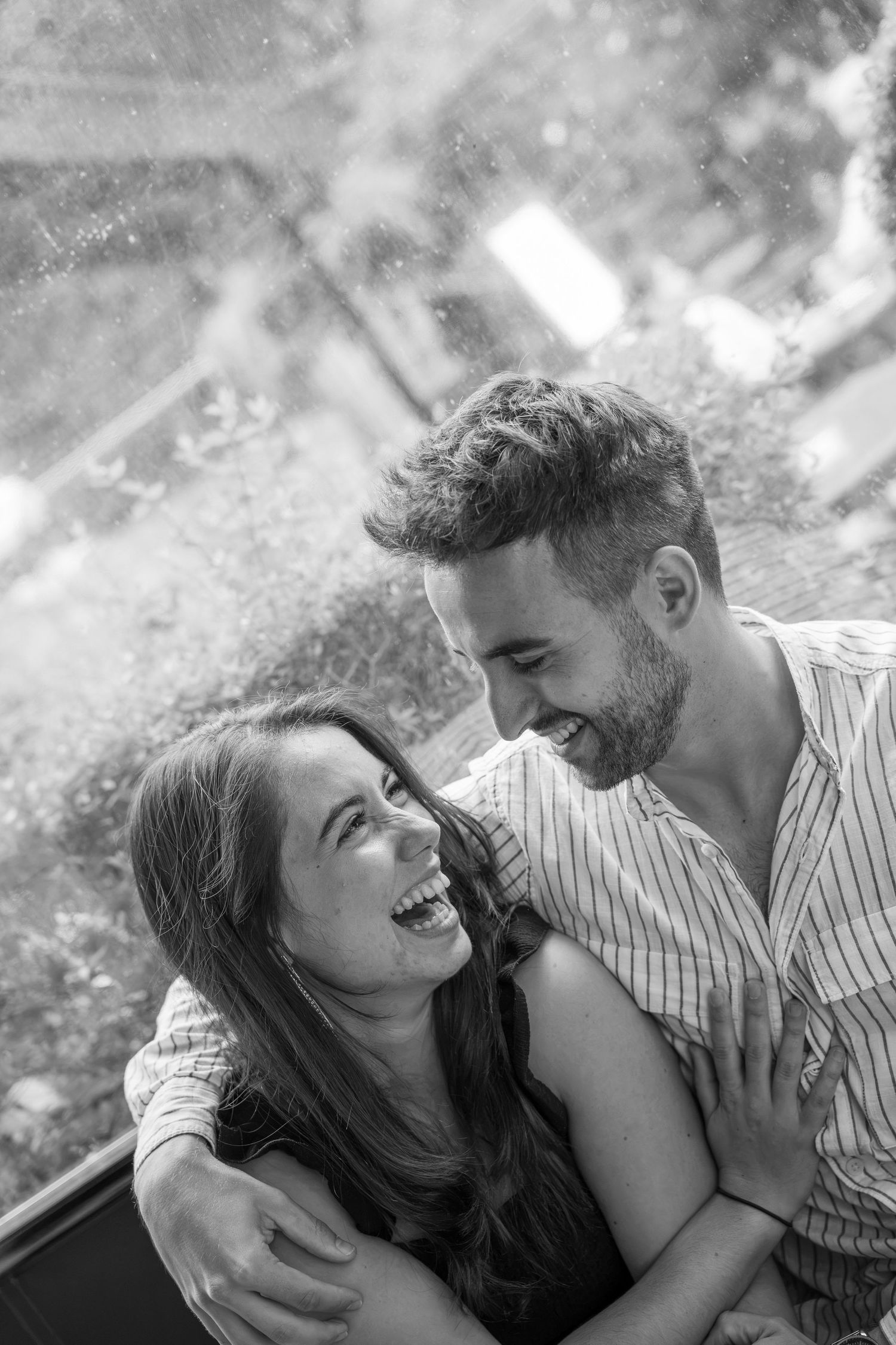 Black and white photo of a laughing couple embracing closely, the bearded man in a striped shirt smiling down at the joyful woman.
