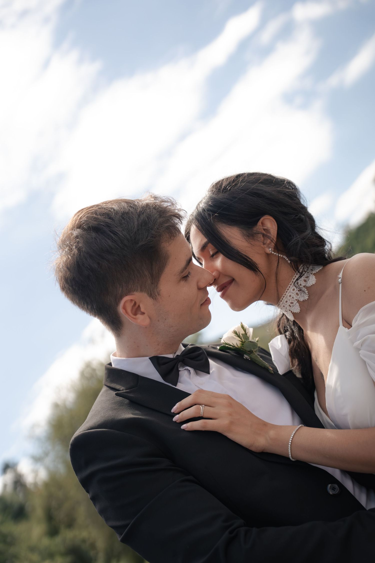 A bride and groom share a romantic moment outdoors, gazing at each other under a blue sky.