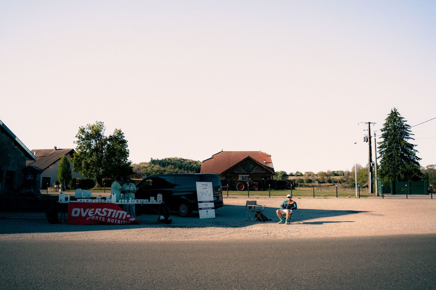 Overstim sports nutrition booth in a sunny open parking area with trees and buildings in the background.