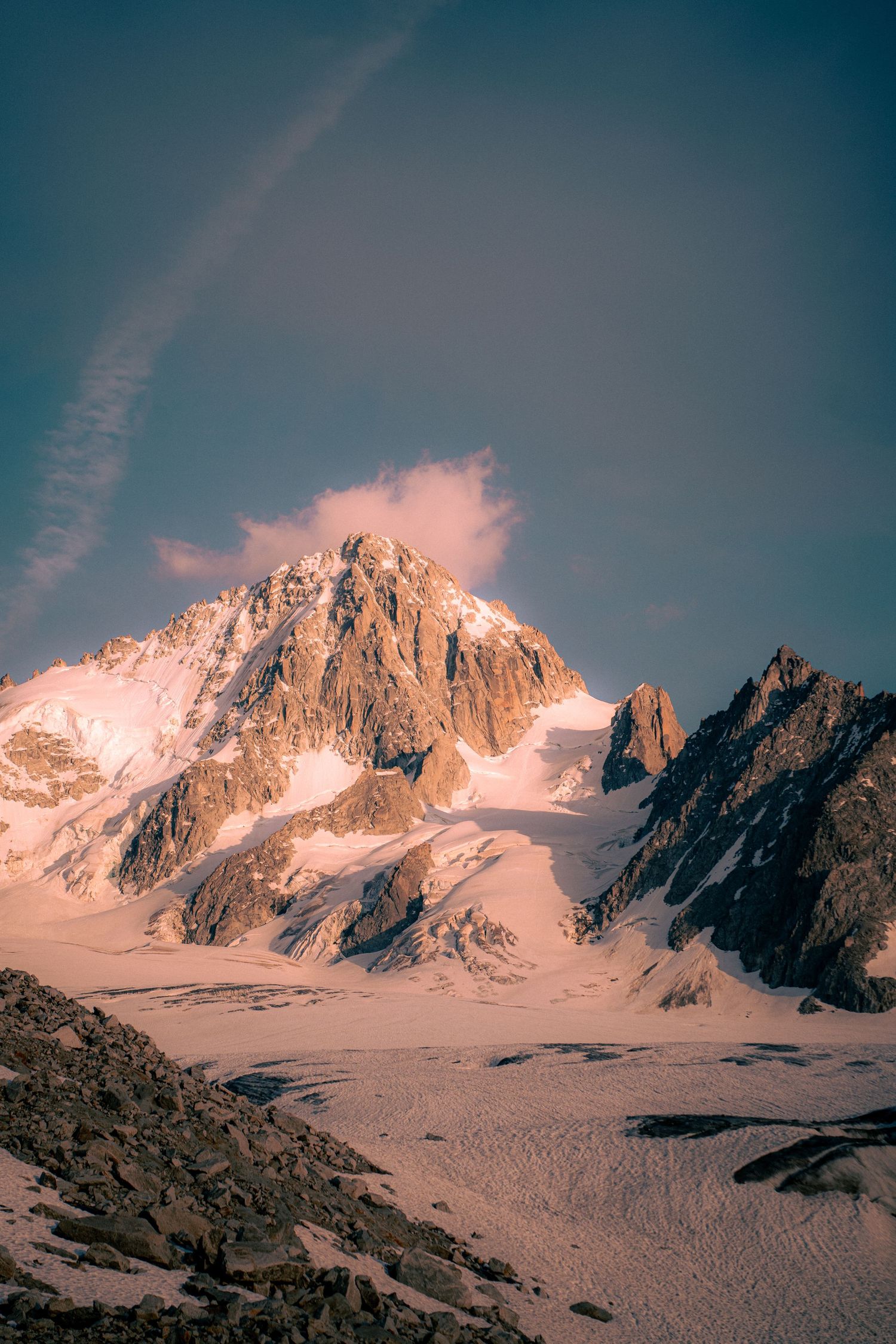 Snow-capped mountain peak bathed in warm sunset light with glacier below and dramatic blue sky.