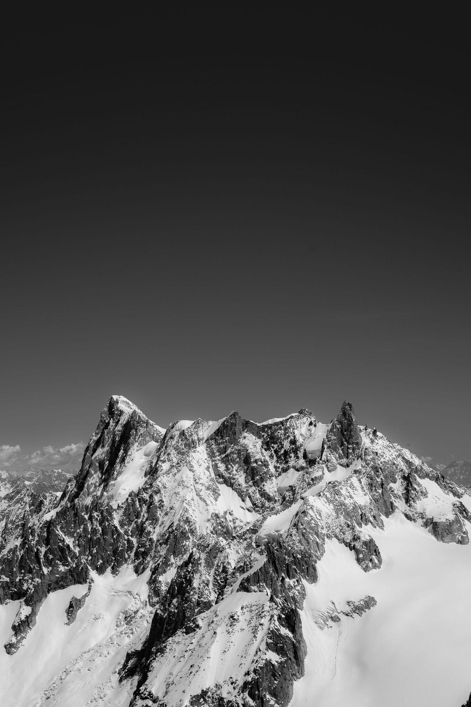 Black and white photo of snow-capped mountain peaks against a dark clear sky.