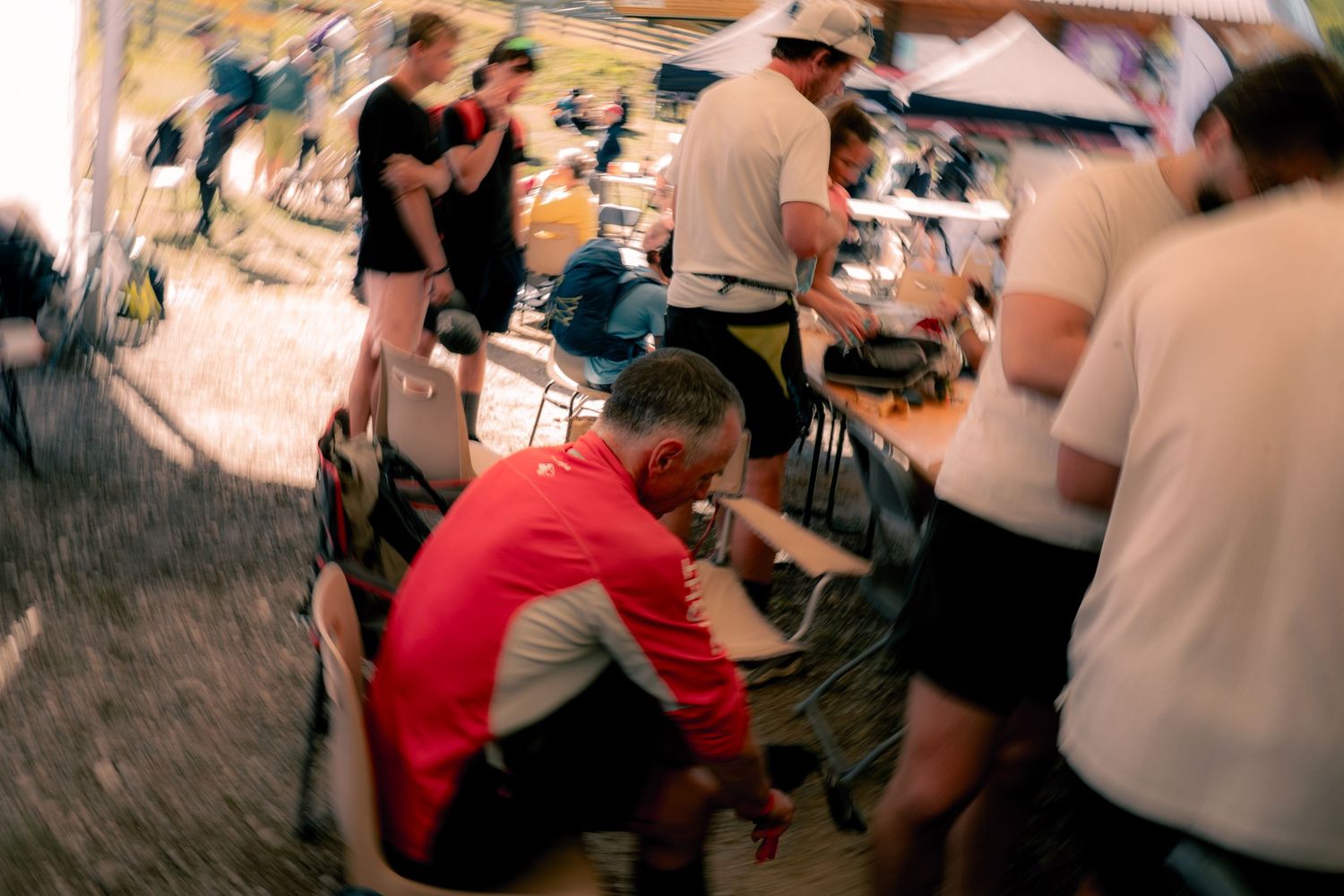 Busy race aid station with runners and crew members tending to gear in a blurred action shot.