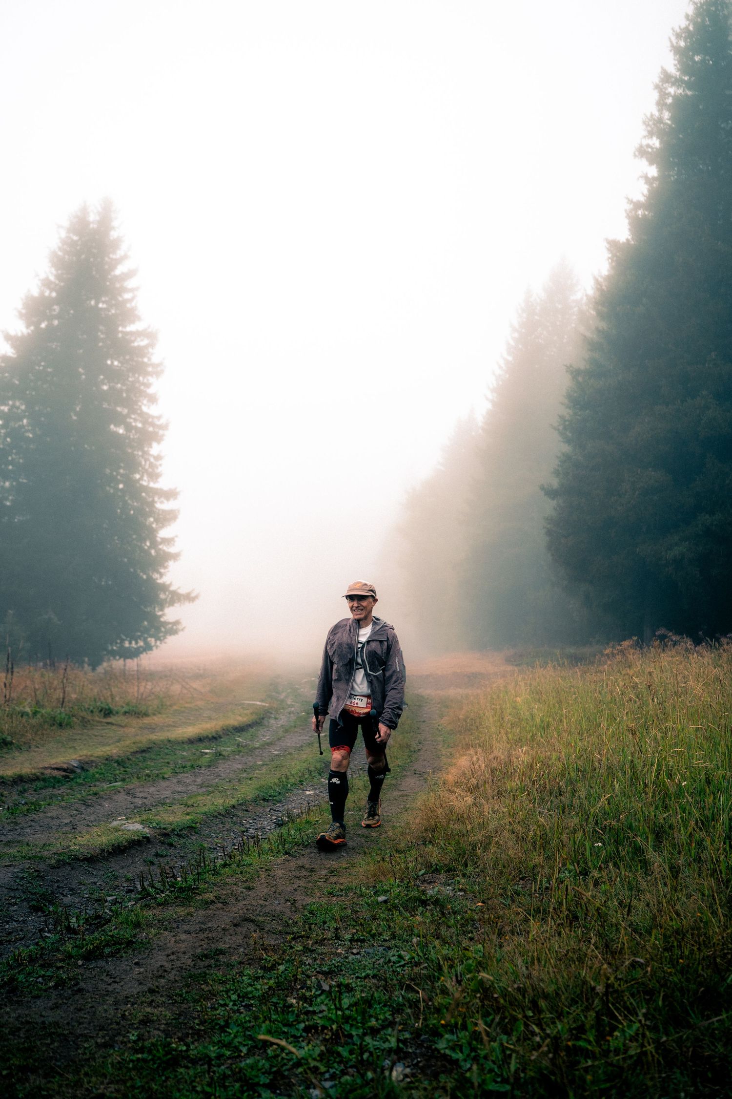 Trail runner stands alone on foggy misty forest path wearing cap and jacket.