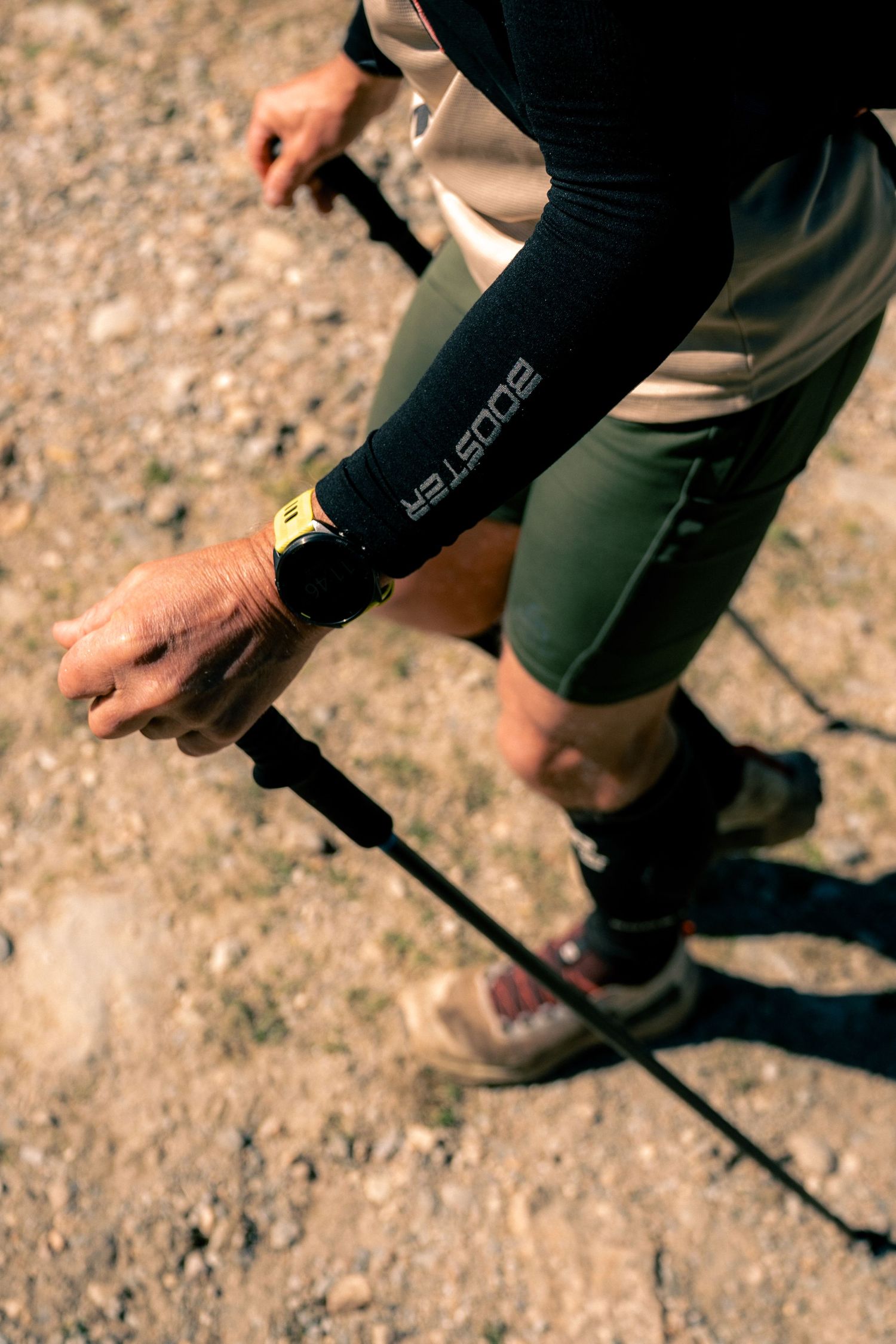 Close-up of hiker's hand gripping trekking pole wearing Booster compression sleeve and yellow wristband.