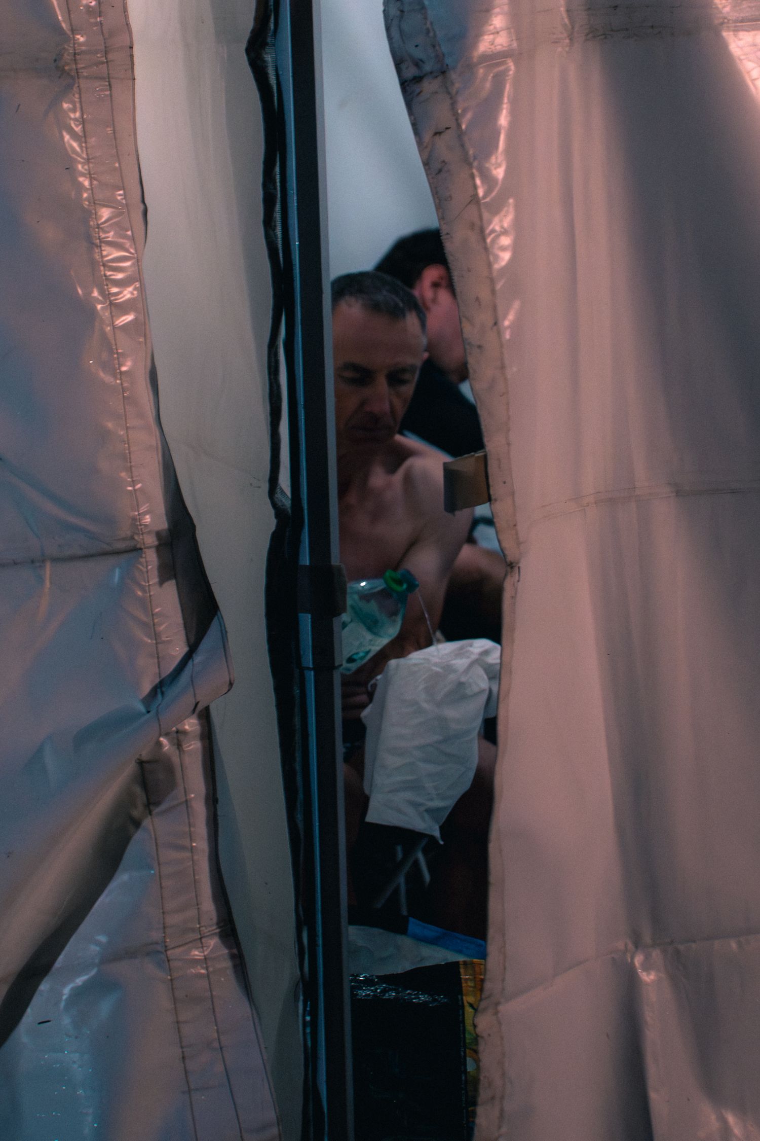 Exhausted trail runner rests inside emergency thermal blanket tent at aid station.
