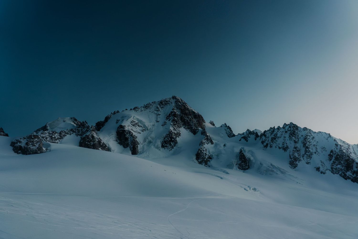 Snow-covered mountain peaks rise against a clear blue sky in this stunning winter alpine landscape photography.